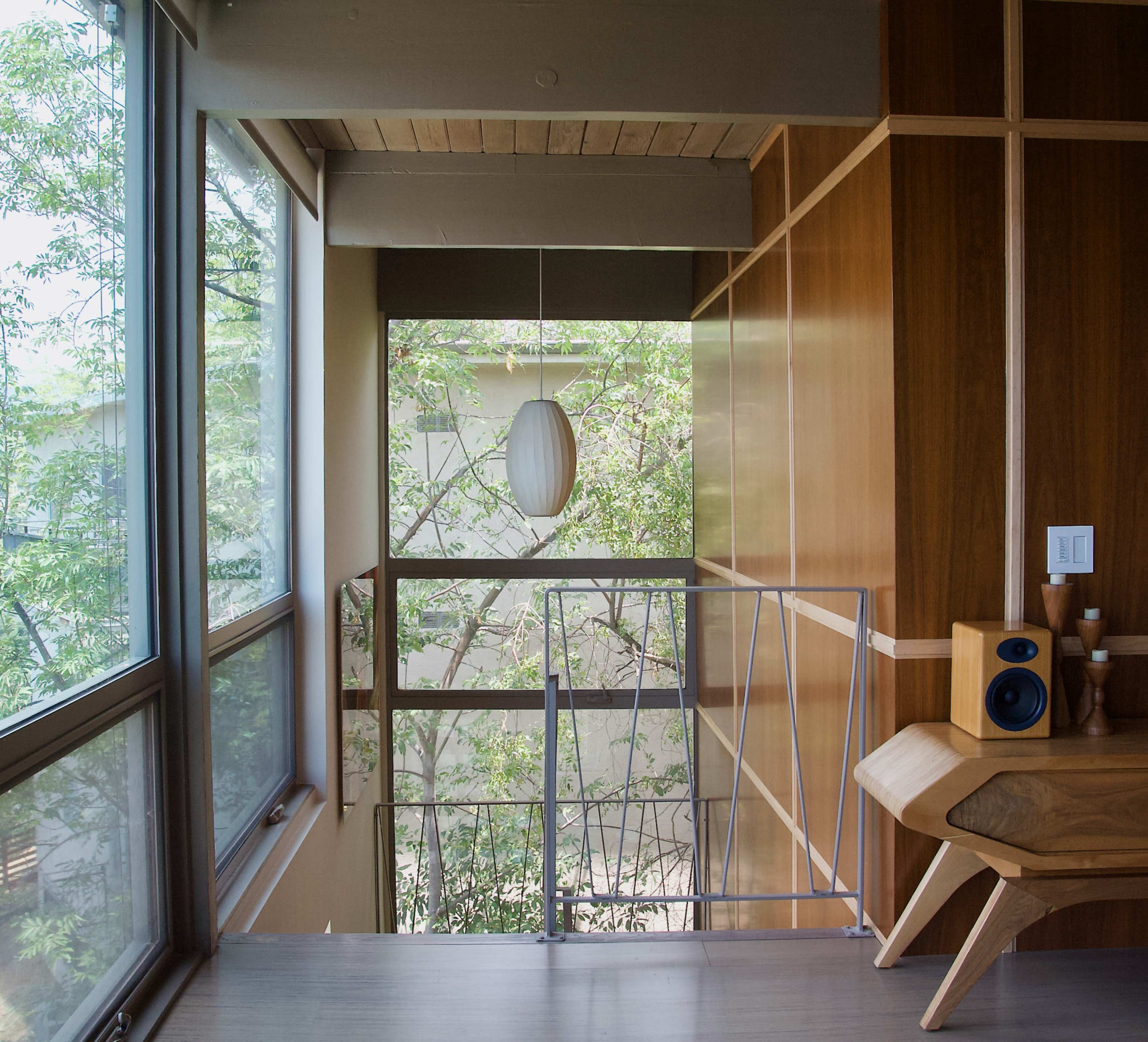 A modern interior features wooden paneling, a light fixture overhead, and large windows with a view of greenery outside.