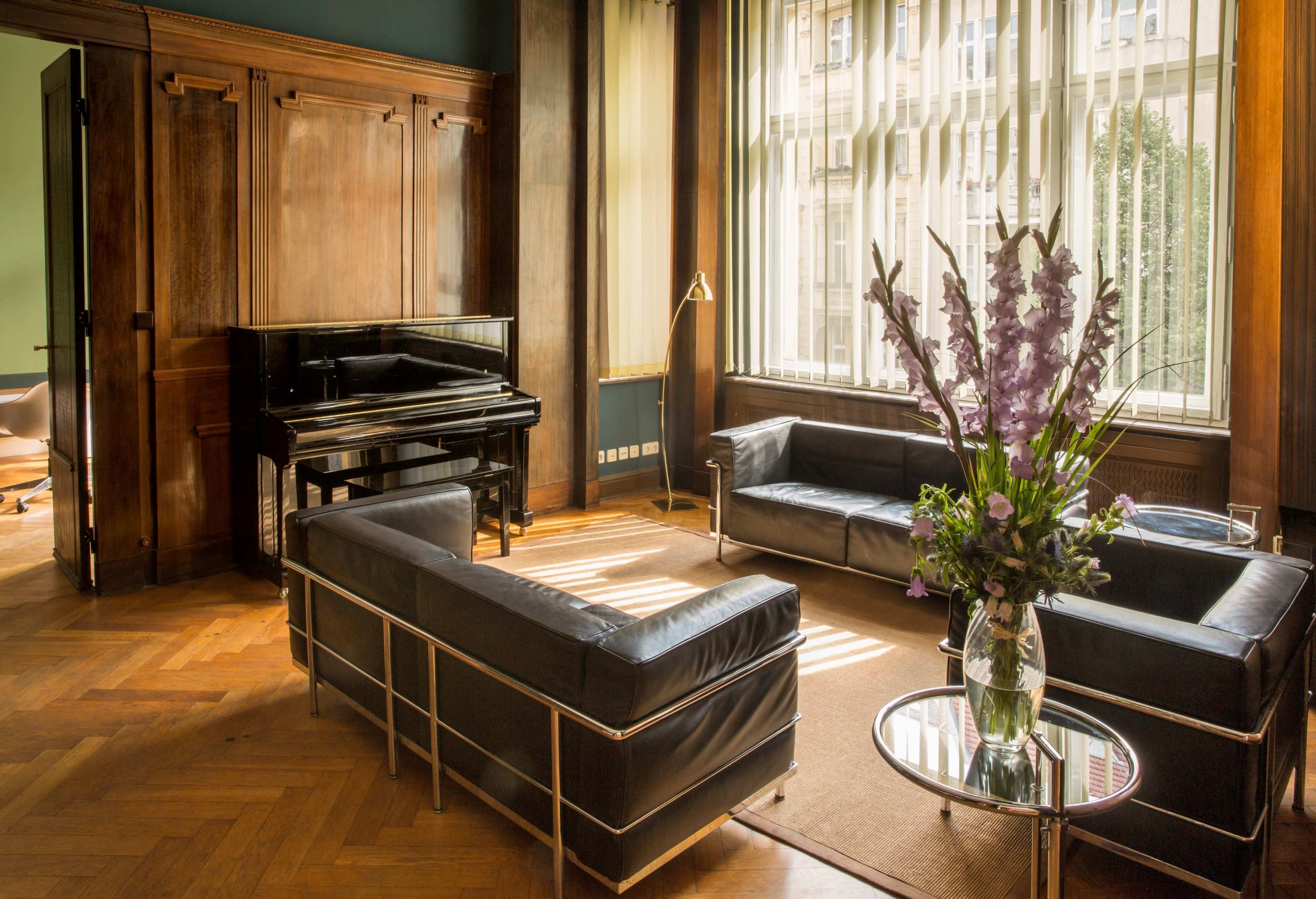 A well-lit interior room featuring a black piano, two modern leather sofas, and a glass coffee table with a bouquet of flowers.