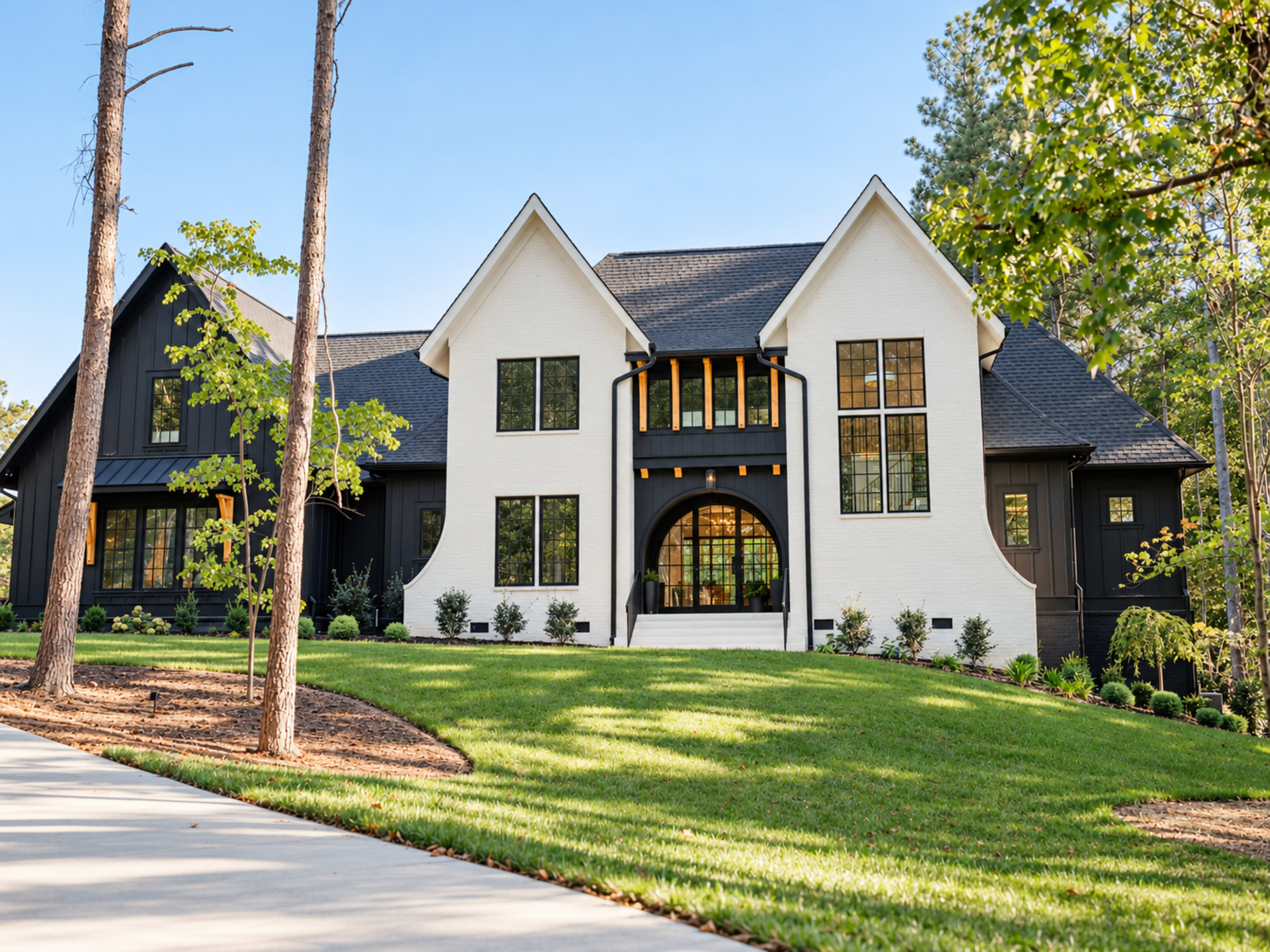 The image shows a large modern two-story house with a combination of white and black exterior, surrounded by a landscaped lawn and trees.