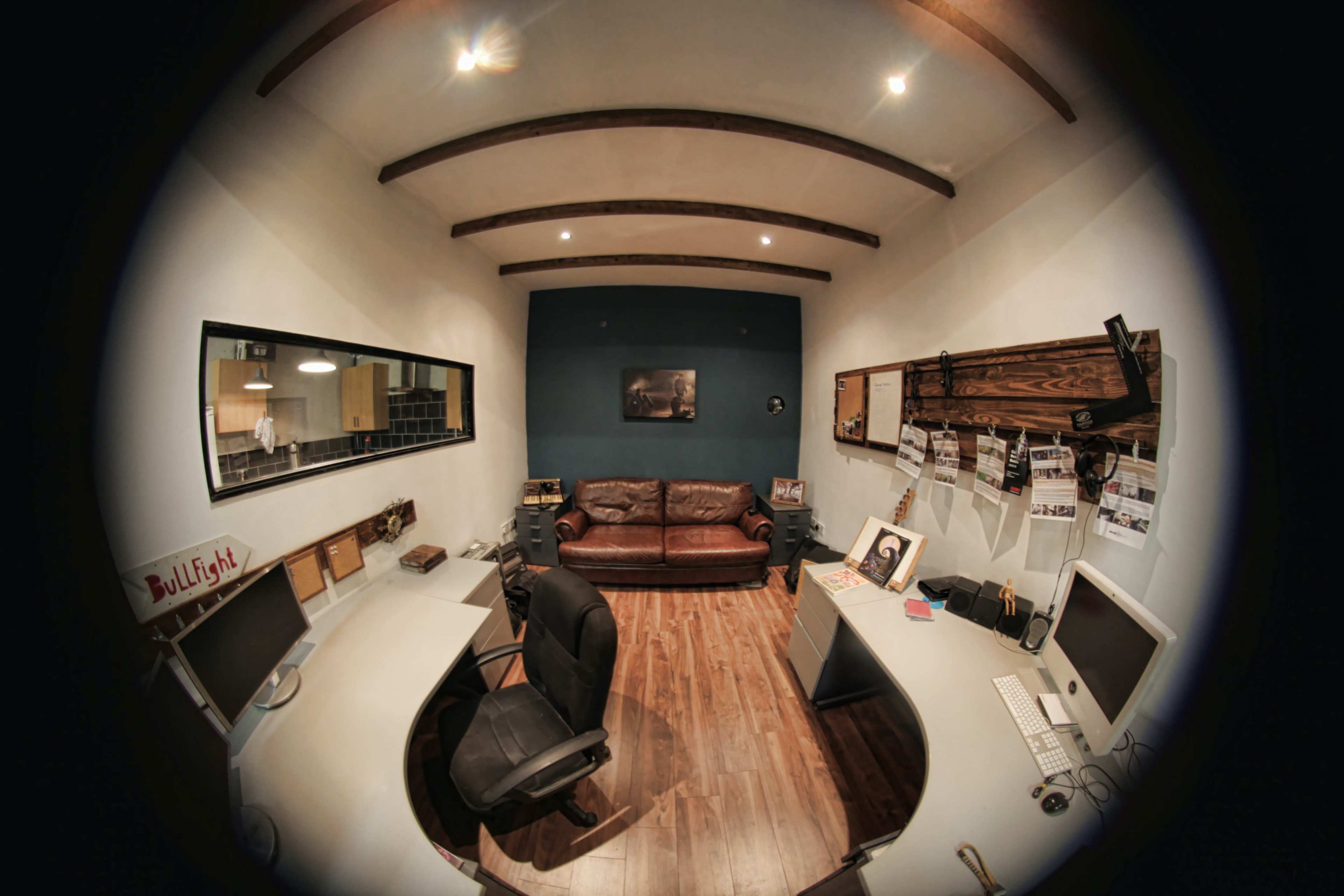 A small office space featuring a brown leather sofa, two workstations with computers, and wooden beams on the ceiling.