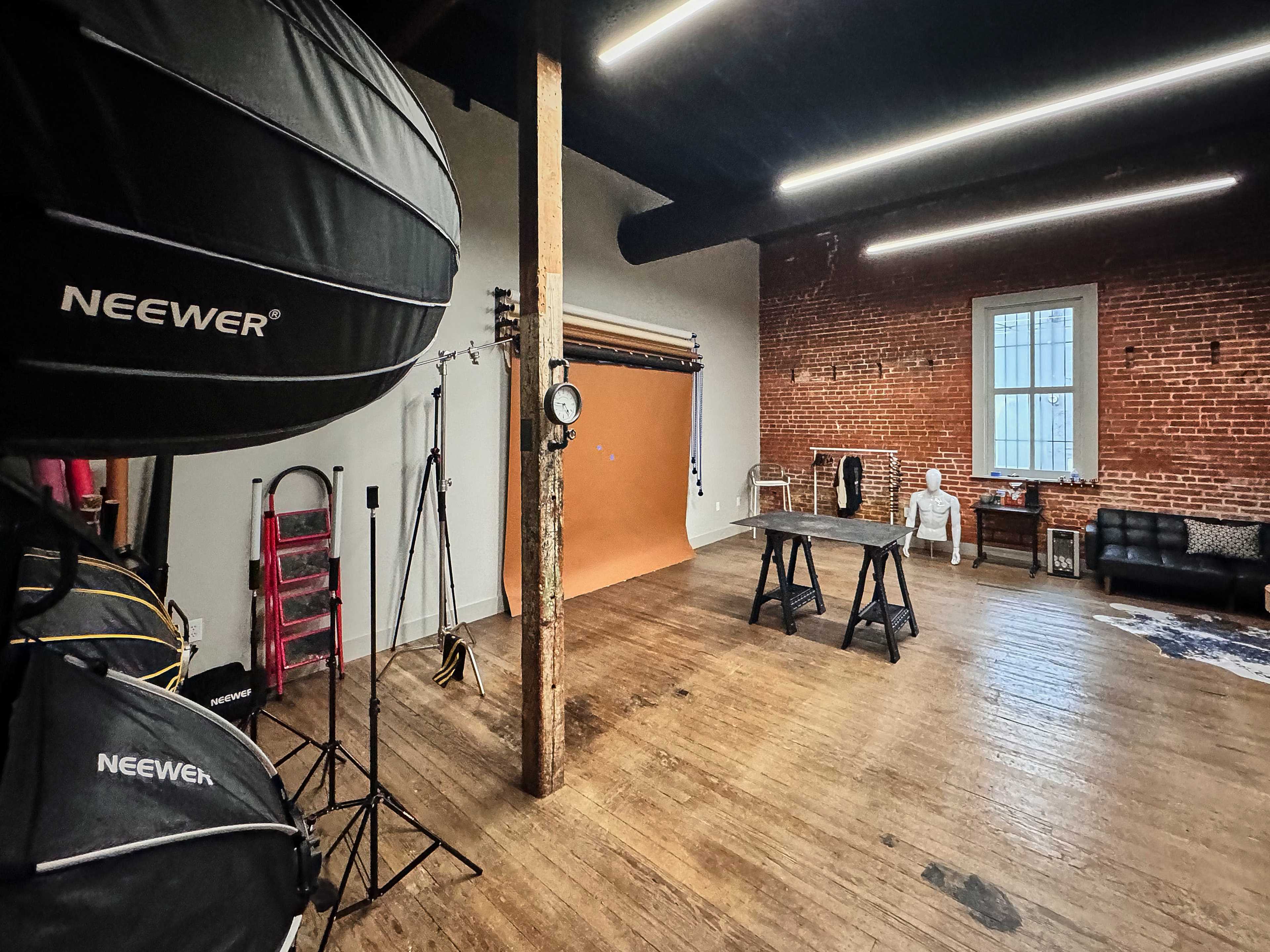 A photo studio featuring brick walls, wooden floors, a backdrop, lighting equipment, and a couch.