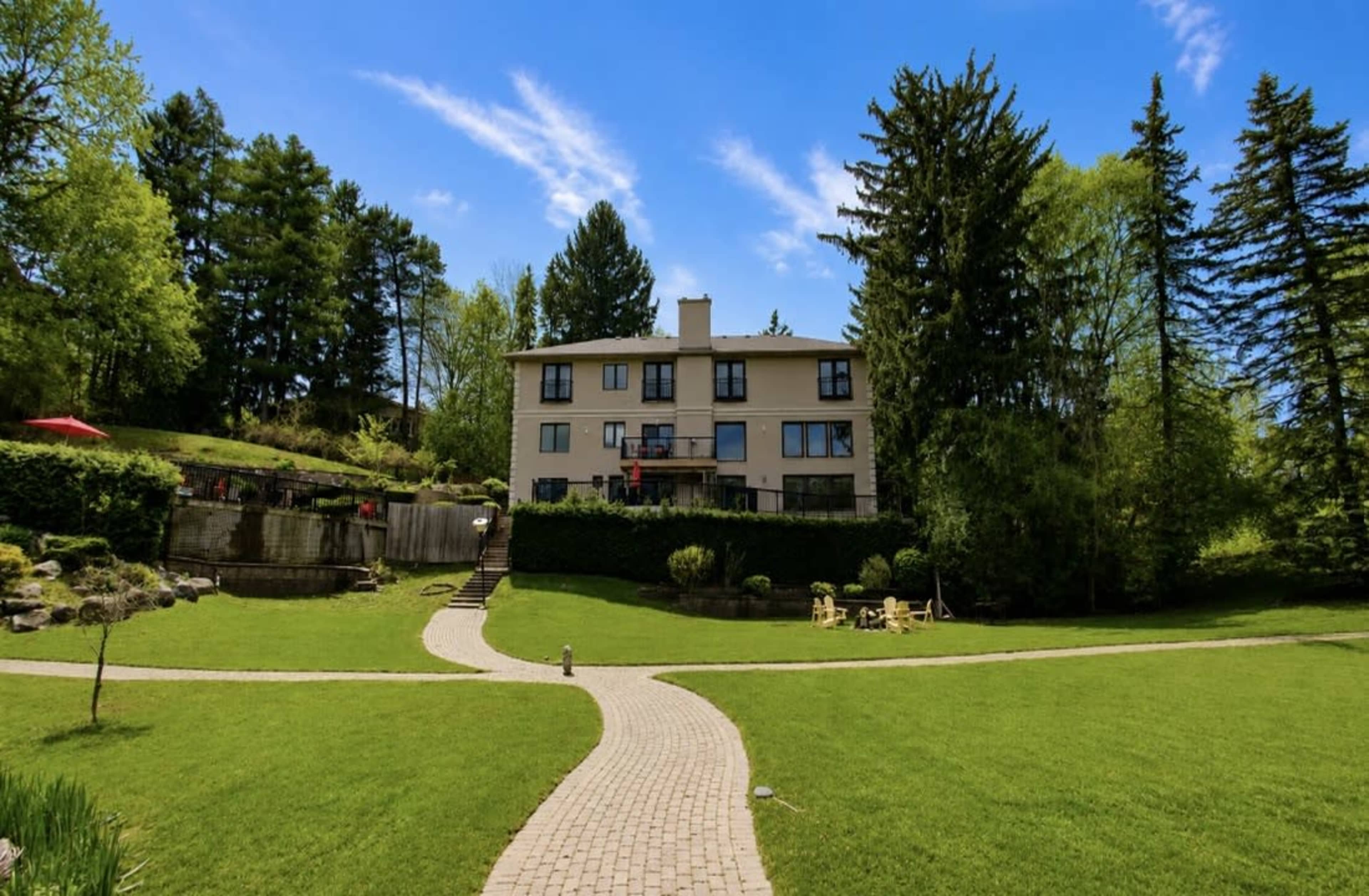 A three-story building stands at the center of a lush green lawn, surrounded by trees and a stone pathway leading to it.