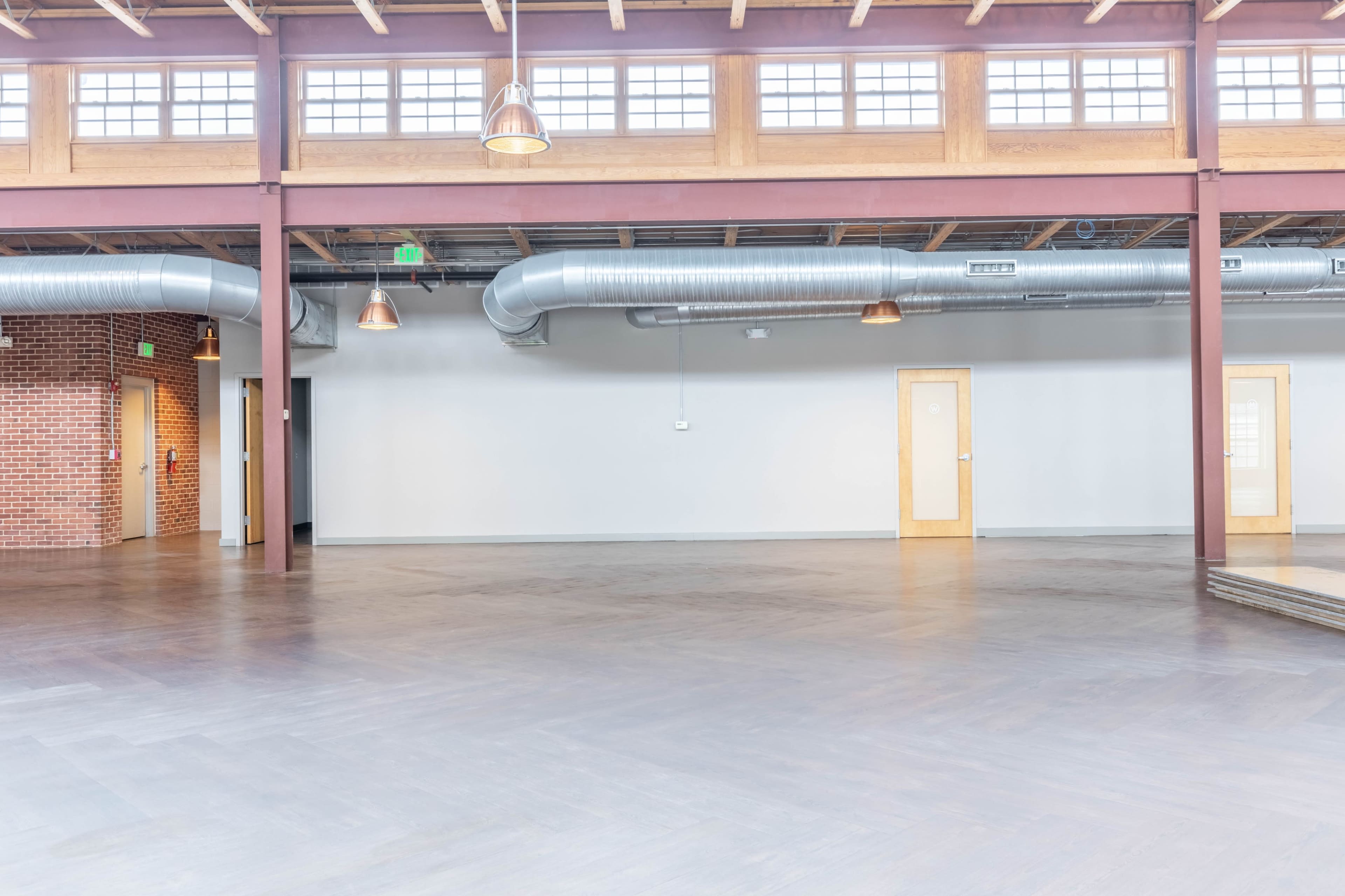 The image shows a spacious, industrial-style interior with high ceilings, large windows, and exposed ducts.