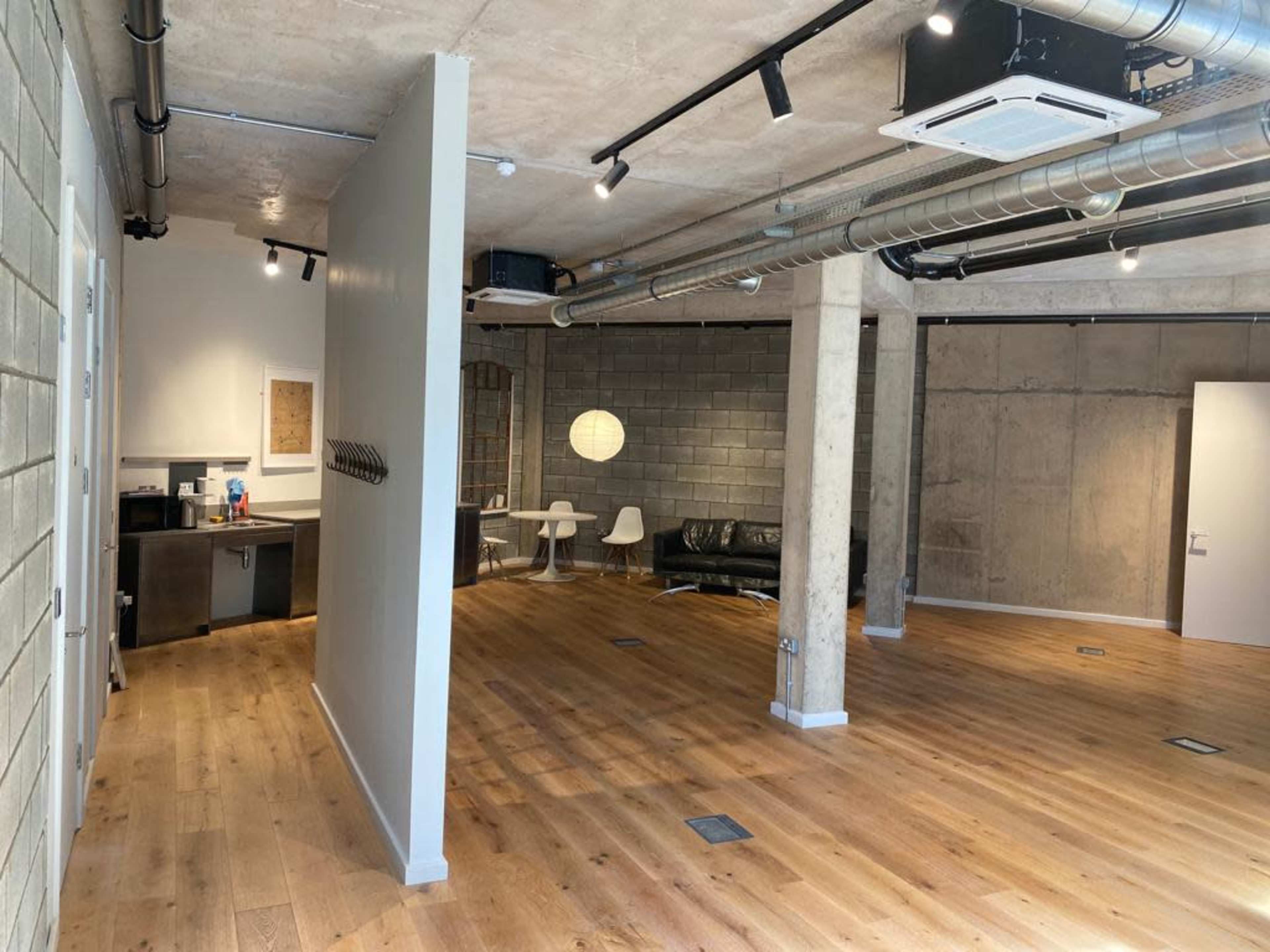 An open interior space with wooden flooring, exposed concrete walls, and modern furniture.