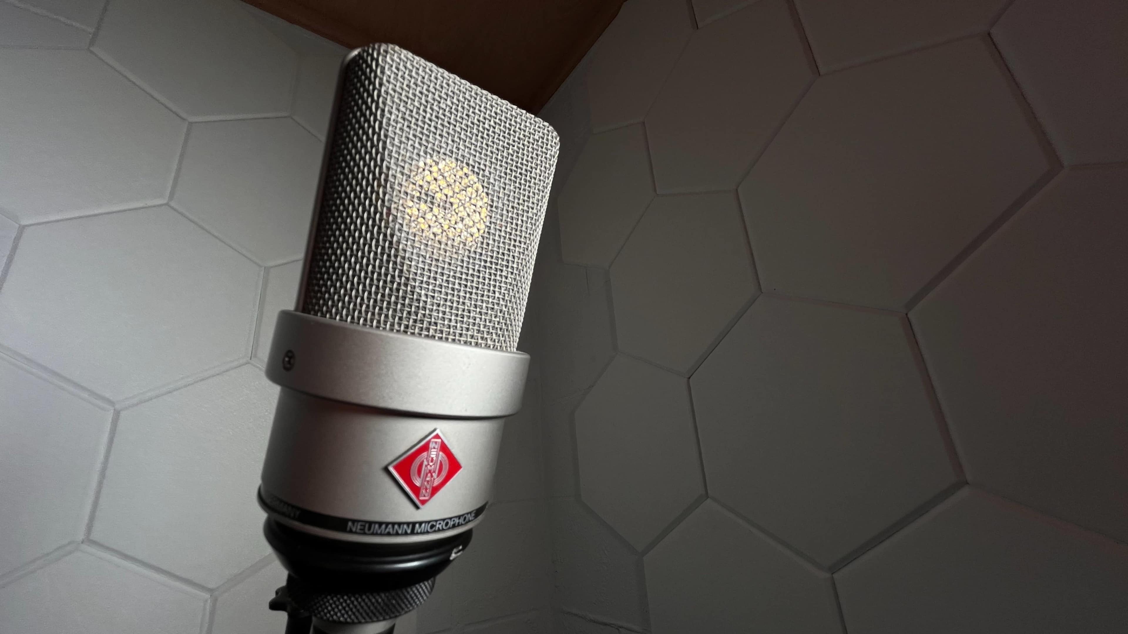 A silver microphone with a mesh grille is positioned against a textured, hexagon-patterned wall.