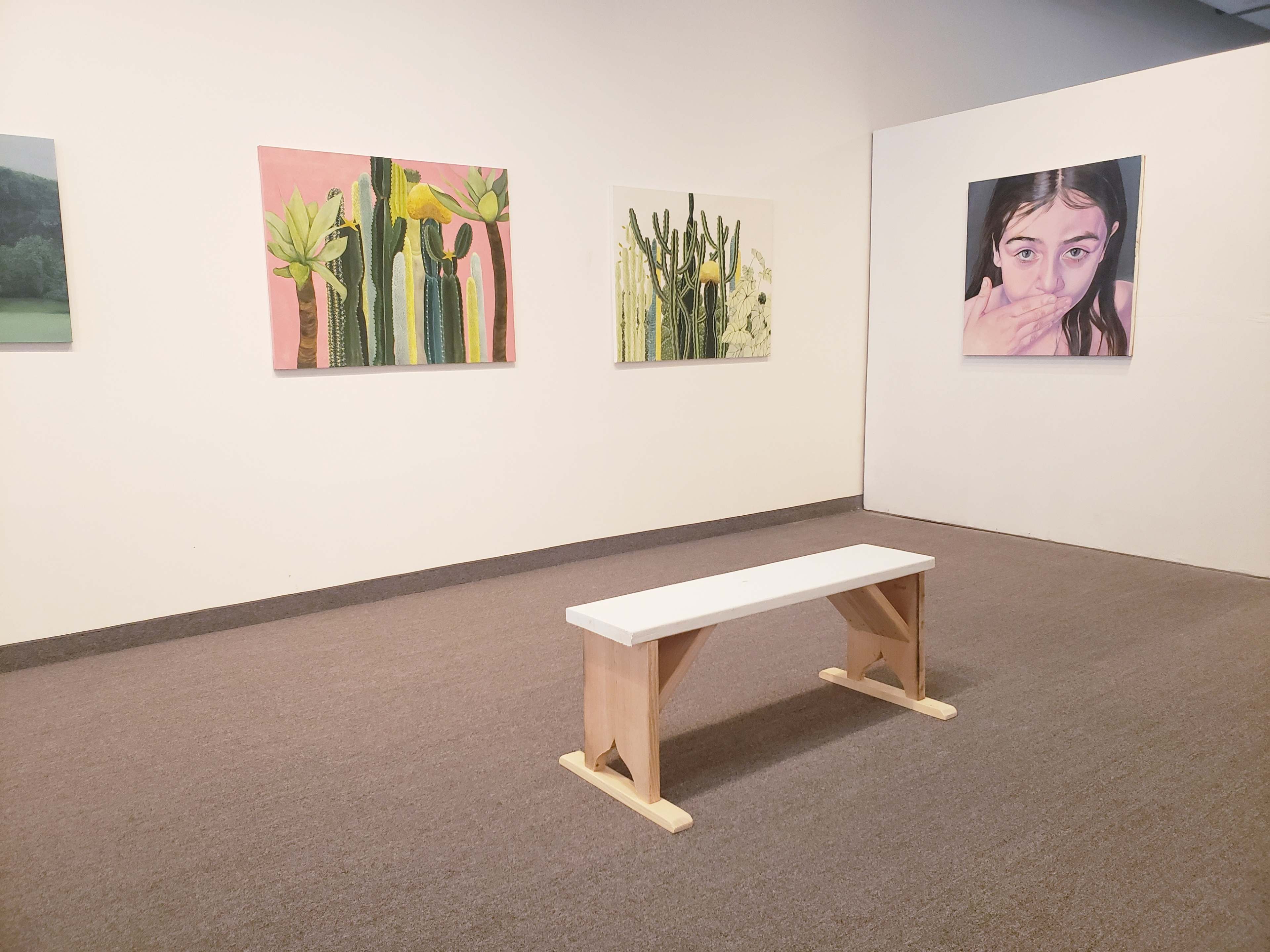 A minimalist art gallery featuring a white wooden bench and four framed artworks on the walls, including cacti and a portrait.