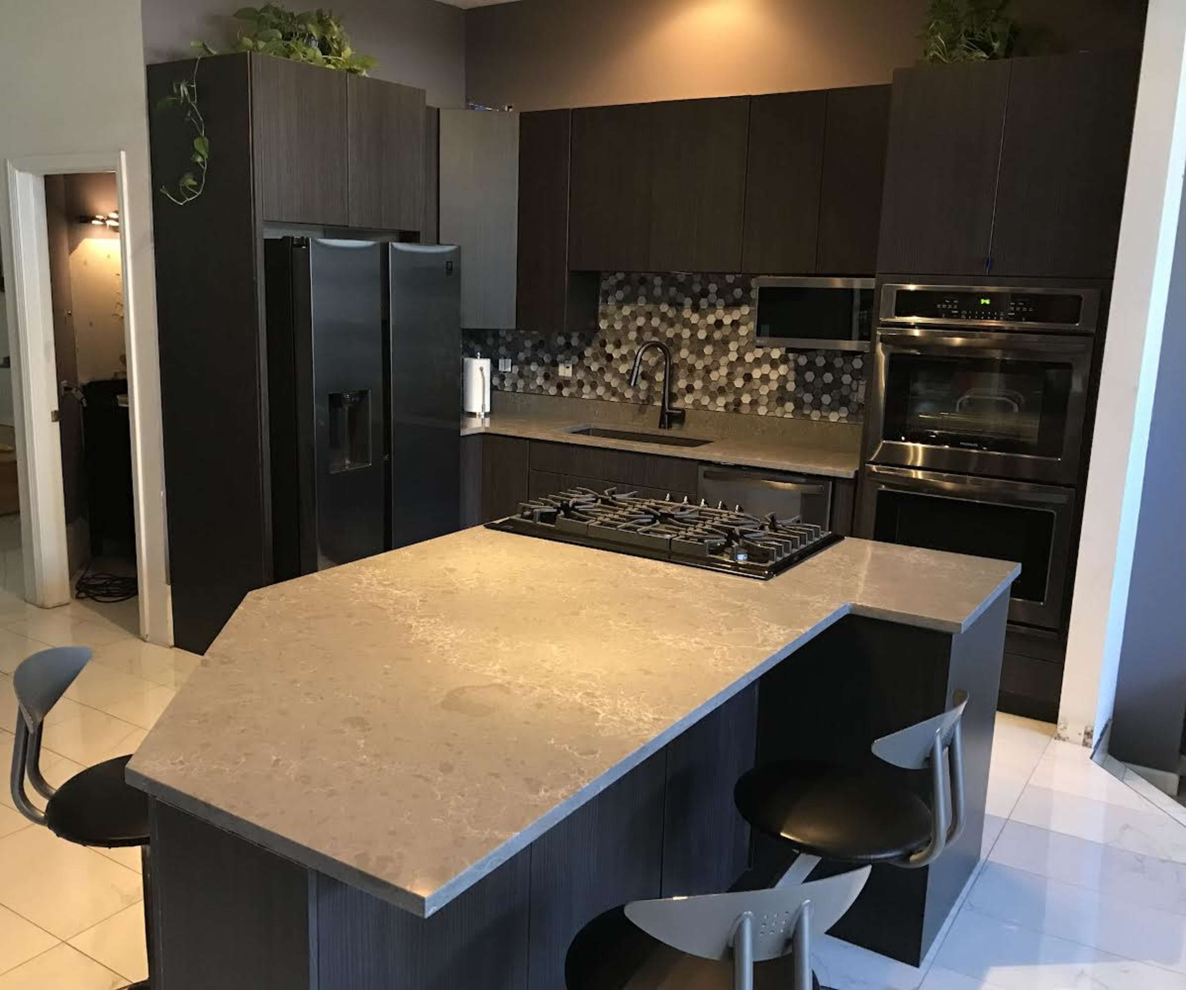 A modern kitchen with dark cabinetry, stainless steel appliances, and a large island with a gas cooktop.
