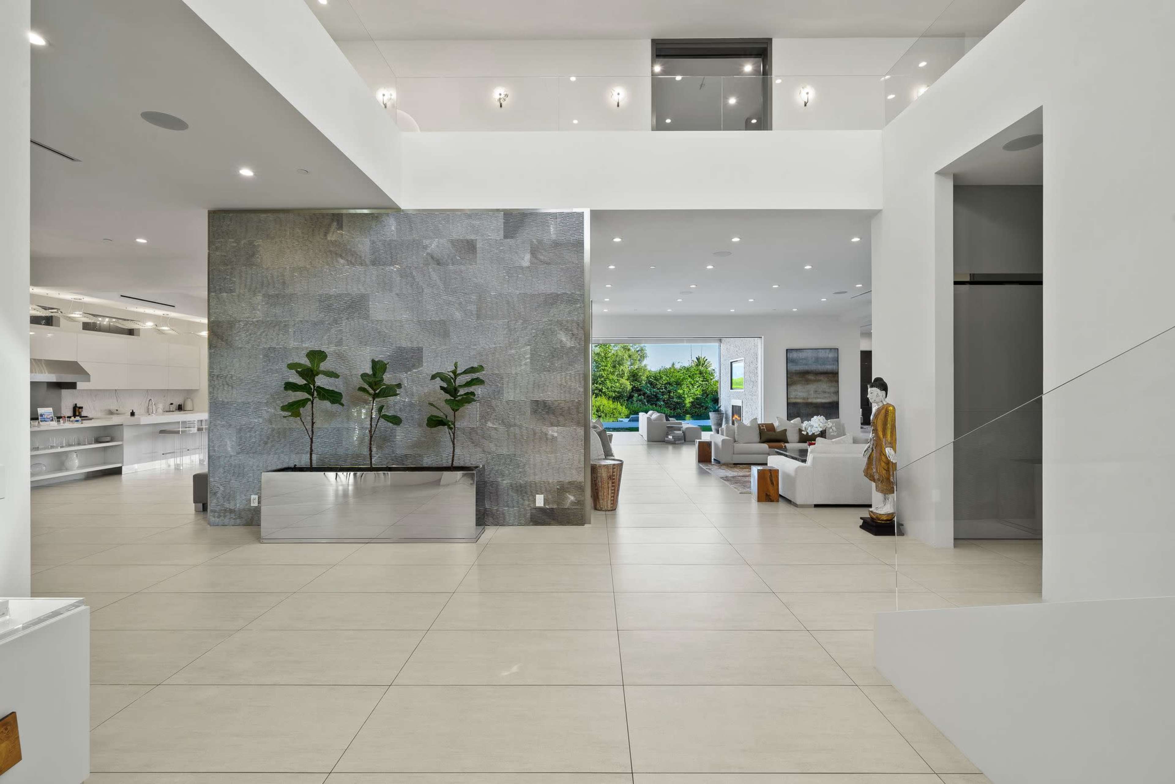 A spacious, modern interior of a home featuring white walls, large windows, and an open layout with a dining area and living room visible in the background.