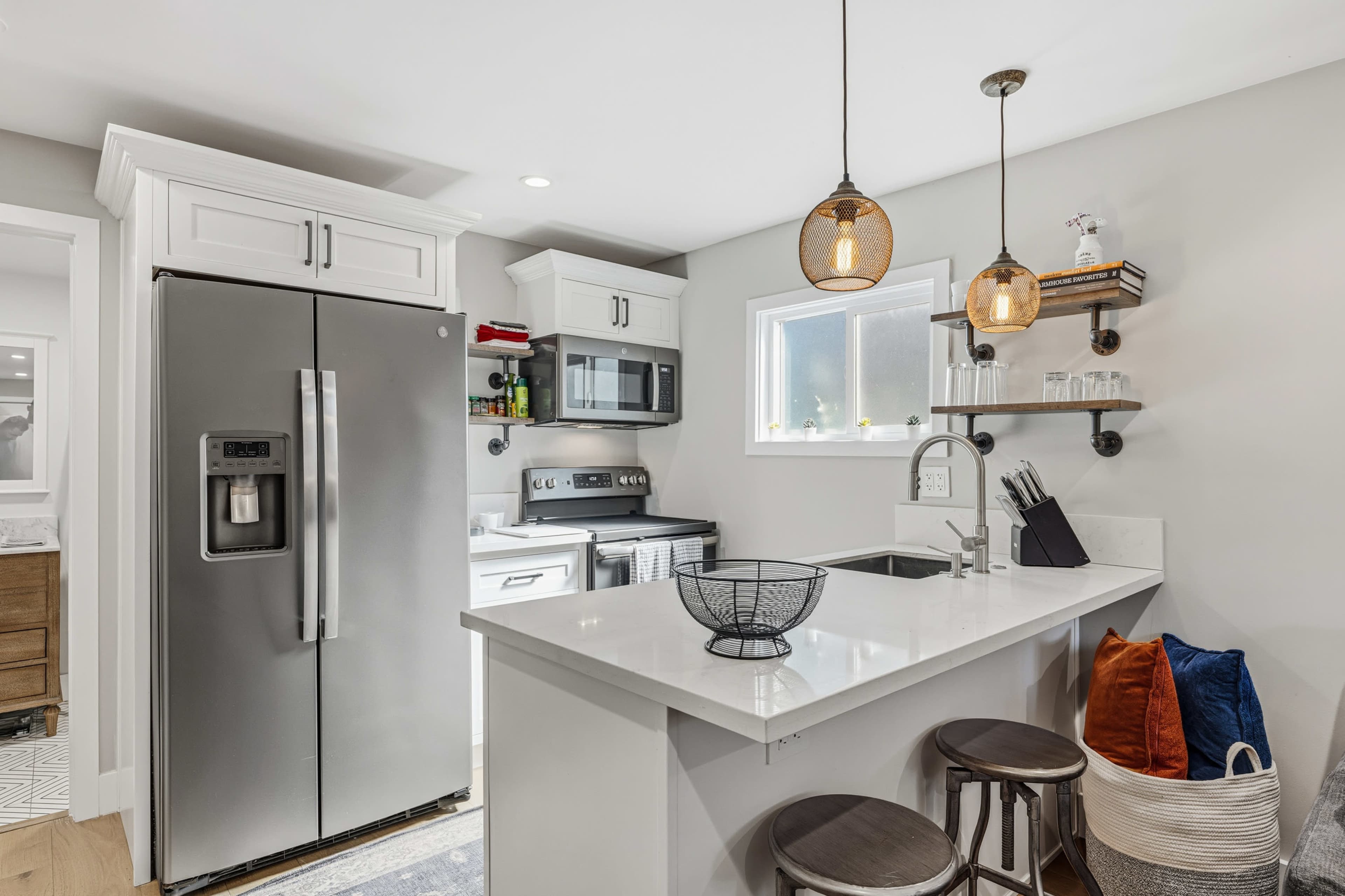 The image shows a modern kitchen with stainless steel appliances, white cabinetry, and a small island featuring bar stools.