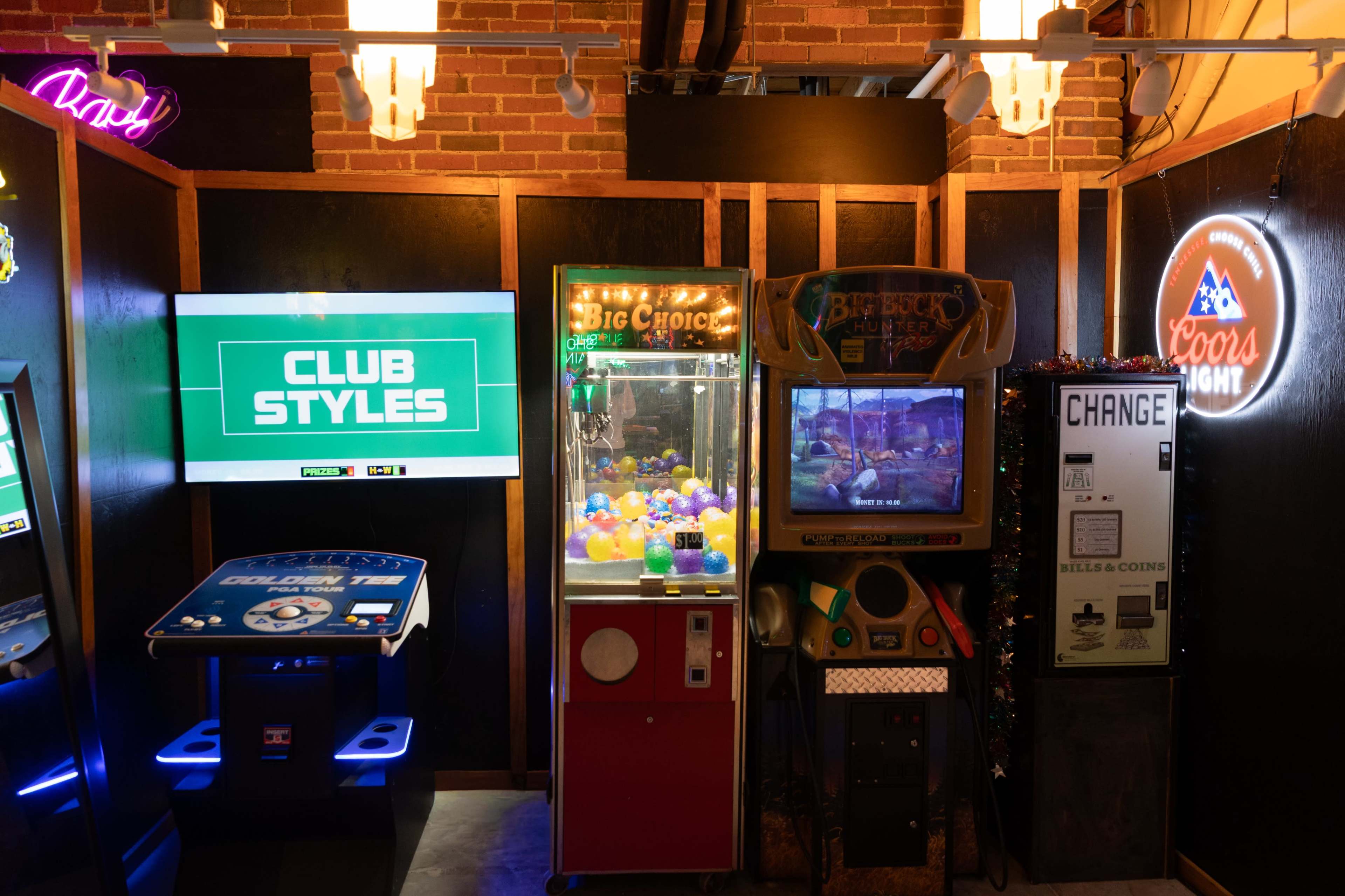 The image shows an arcade area featuring a game cabinet labeled "Club Styles," a prize machine filled with colorful balls, a video game console, and a coin change machine.