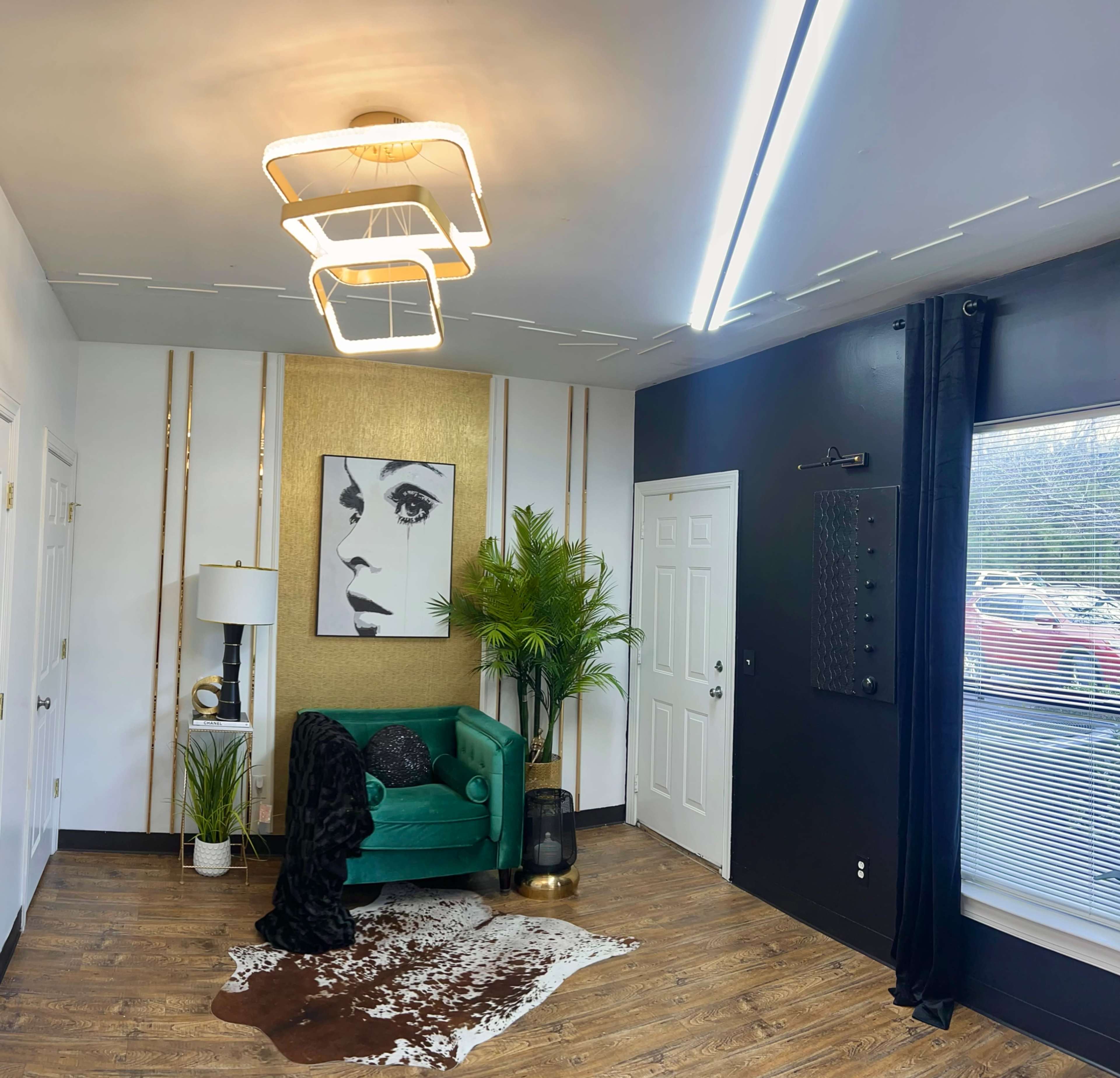 The image features a modern interior with a green sofa, a large portrait of a woman on the wall, and a mix of decorative plants and furniture elements.