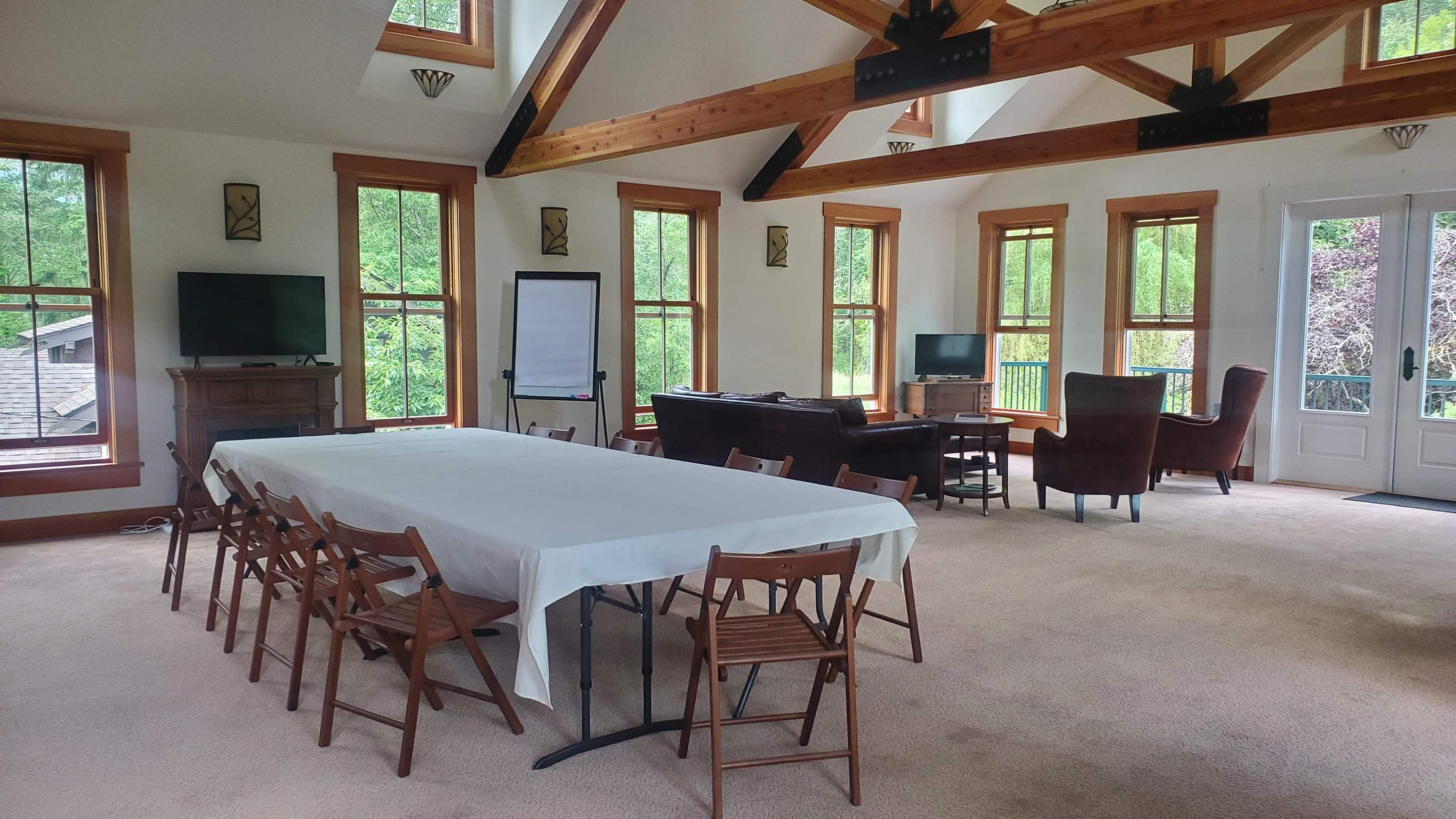 A spacious meeting room features a long table surrounded by chairs, with large windows and wooden beams overhead.