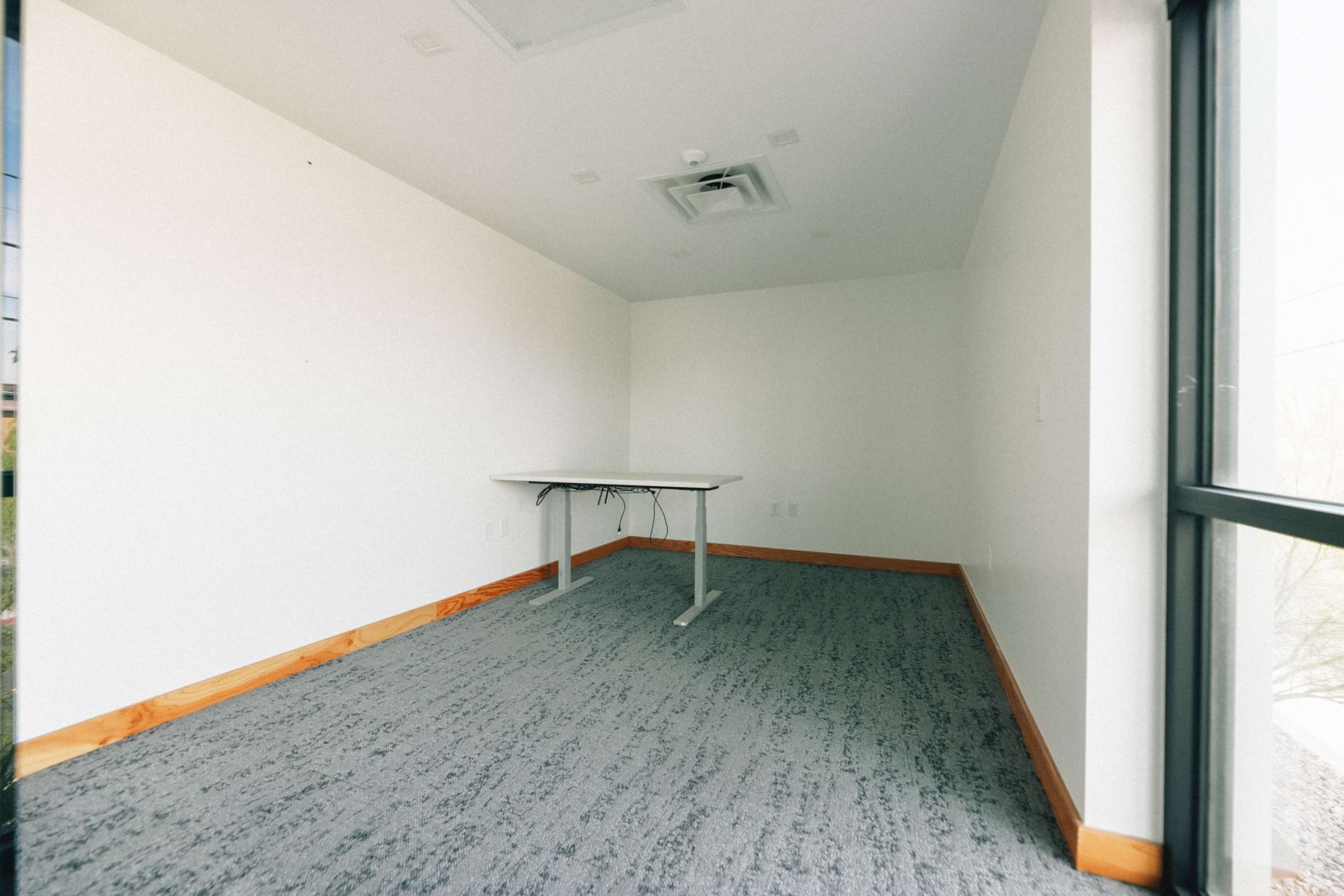 An empty room features a single table against a wall, with gray carpet and white walls.