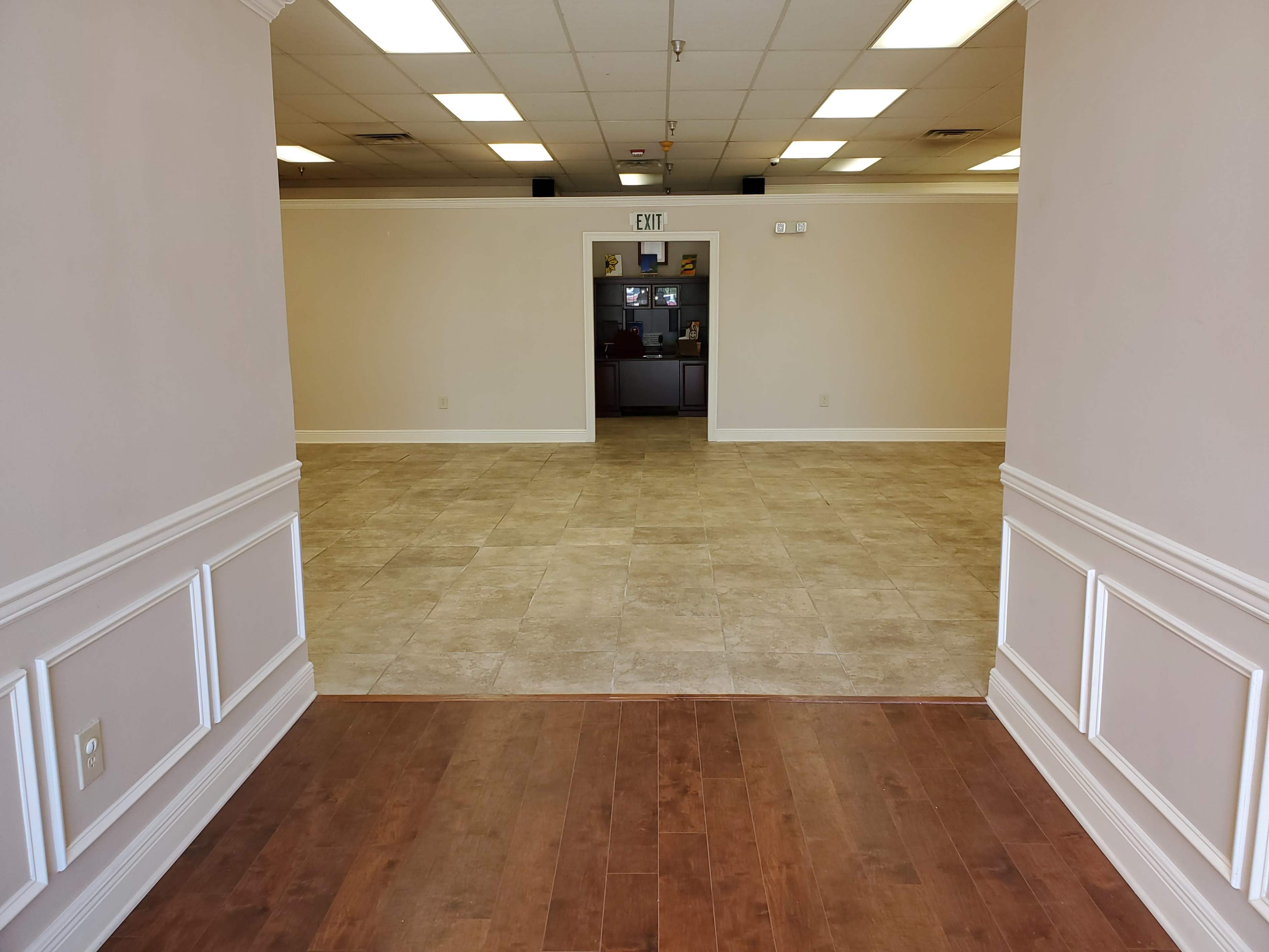 A vacant interior space with a tiled floor and framed walls leading to an exit sign in the background.