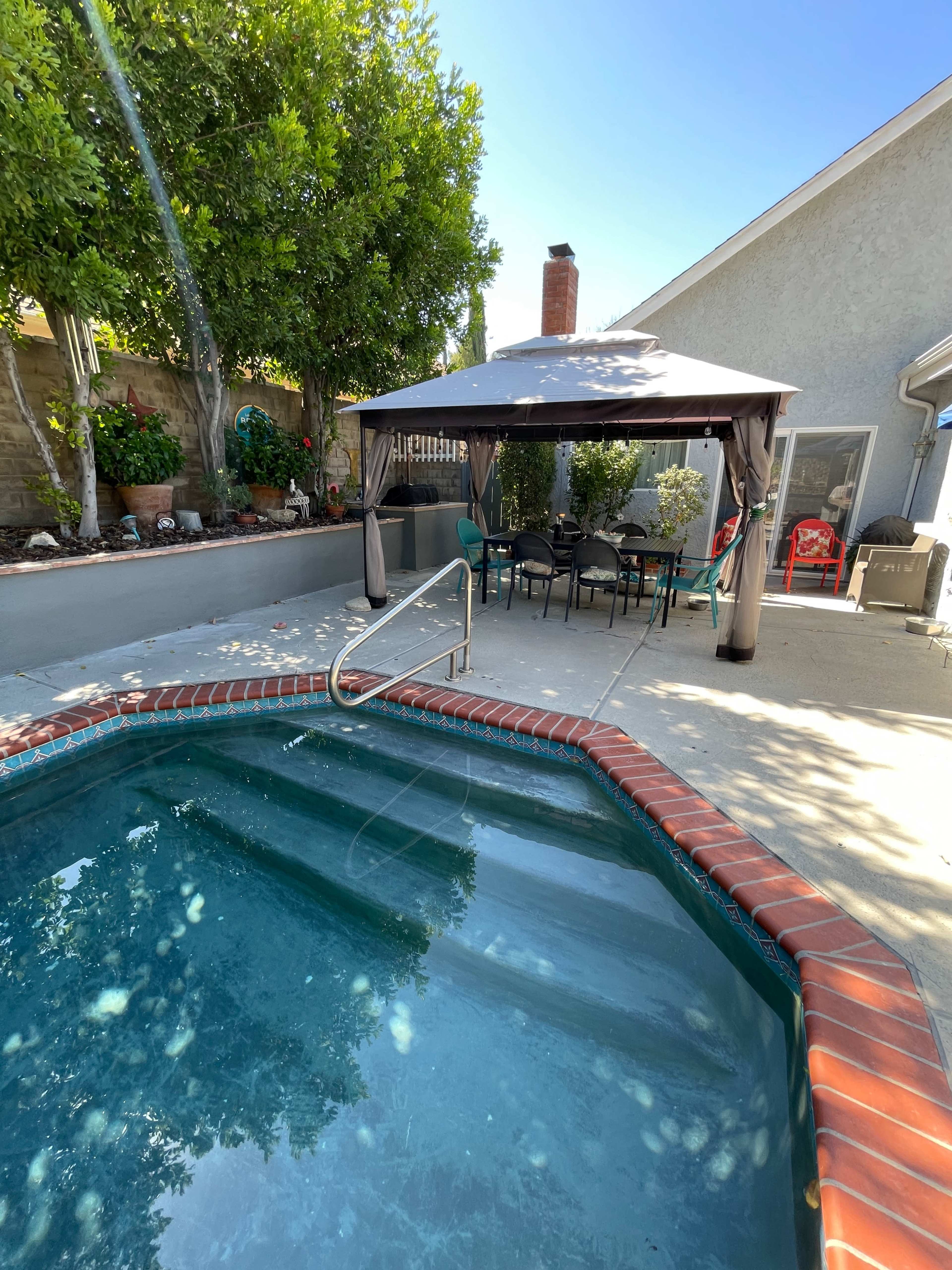 A small pool surrounded by a patio with a gazebo and outdoor seating area.