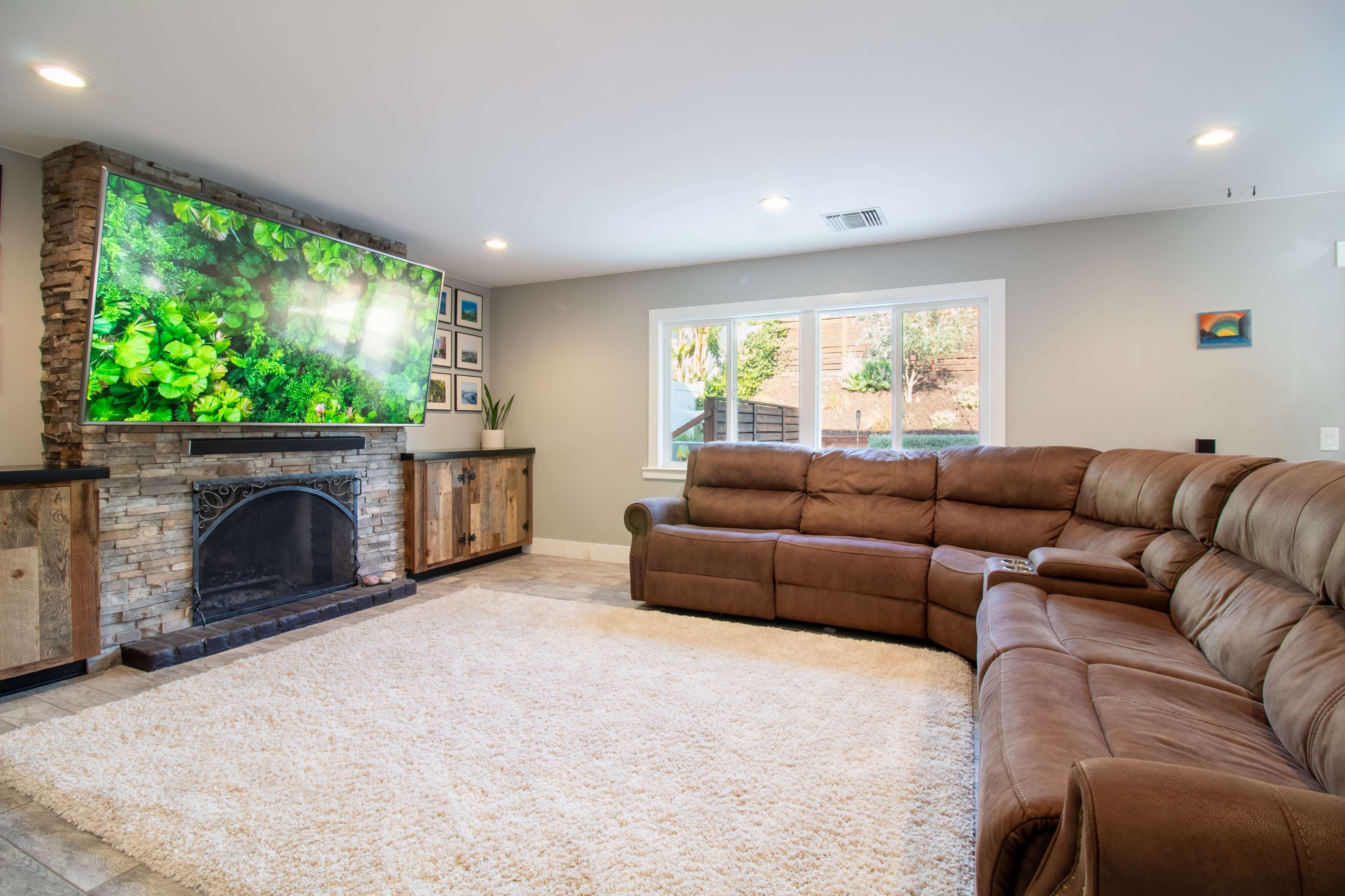 The living room features a large sectional sofa, a stone fireplace, and a wall-mounted television displaying a nature scene, with a plush rug covering the floor.