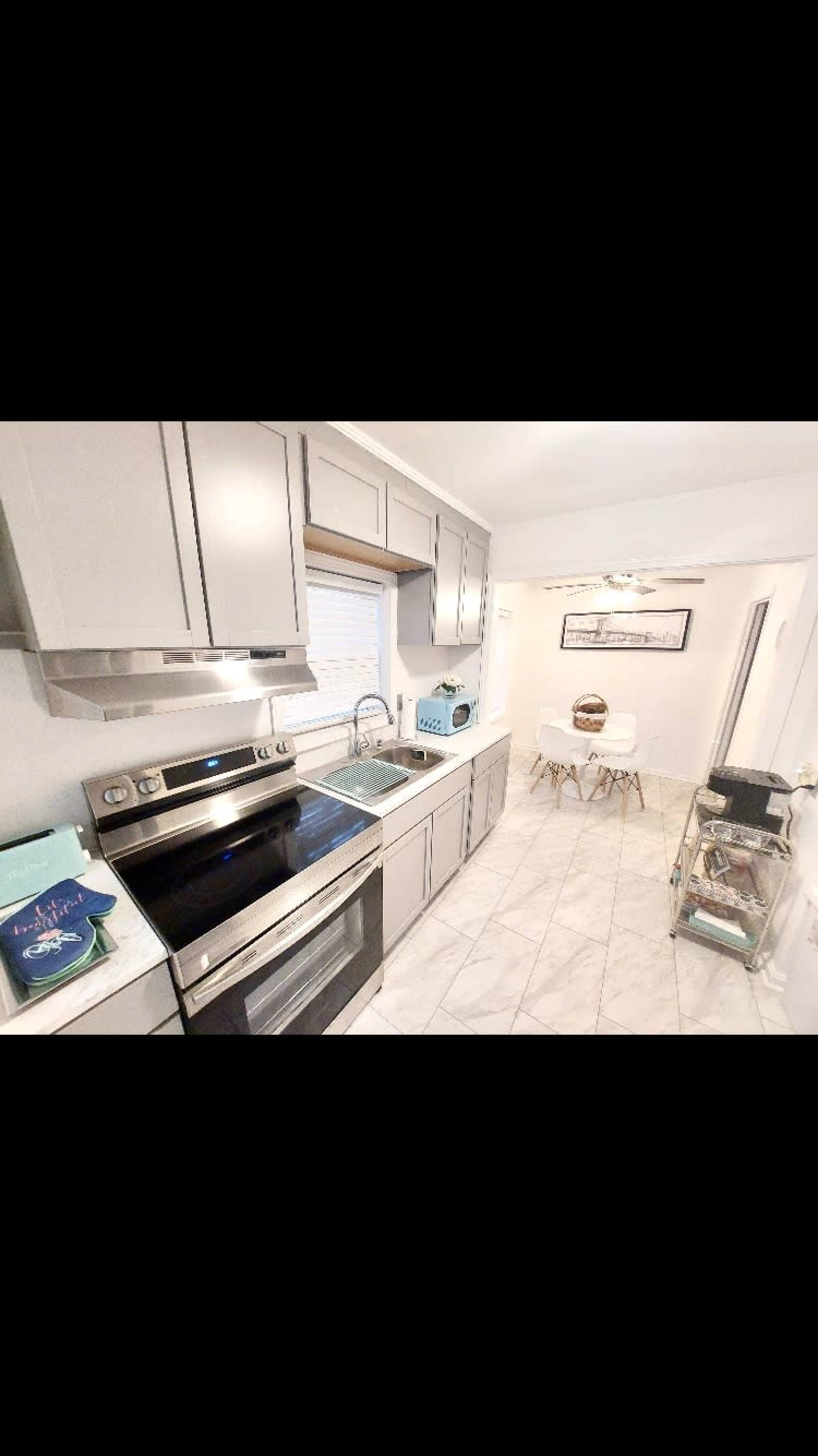 A modern kitchen with gray cabinetry, stainless steel appliances, and a small dining area featuring a round table and chairs.