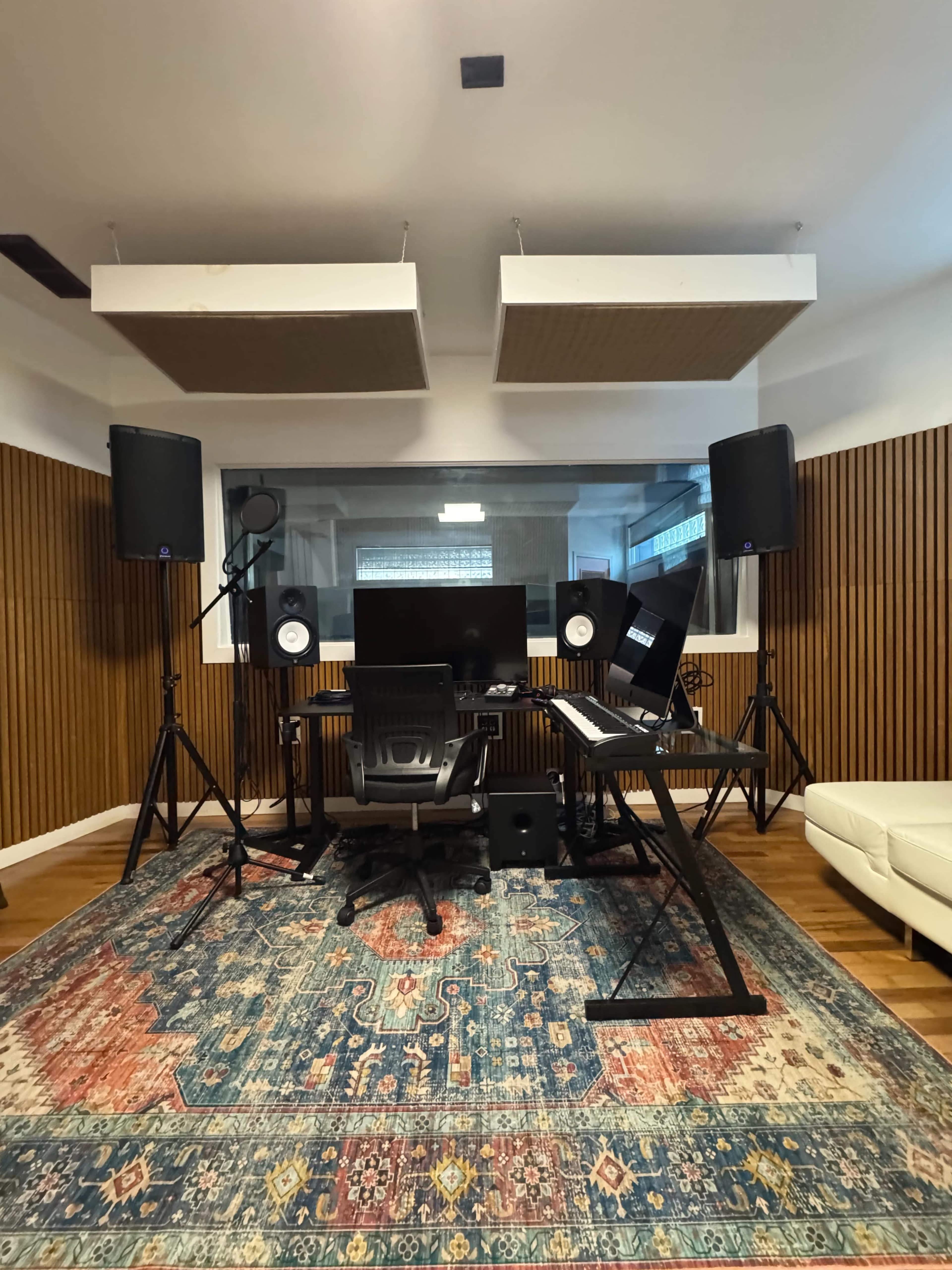The image shows a modern music studio with a large desk, two speakers on stands, a computer monitor, and acoustic panels on the walls.