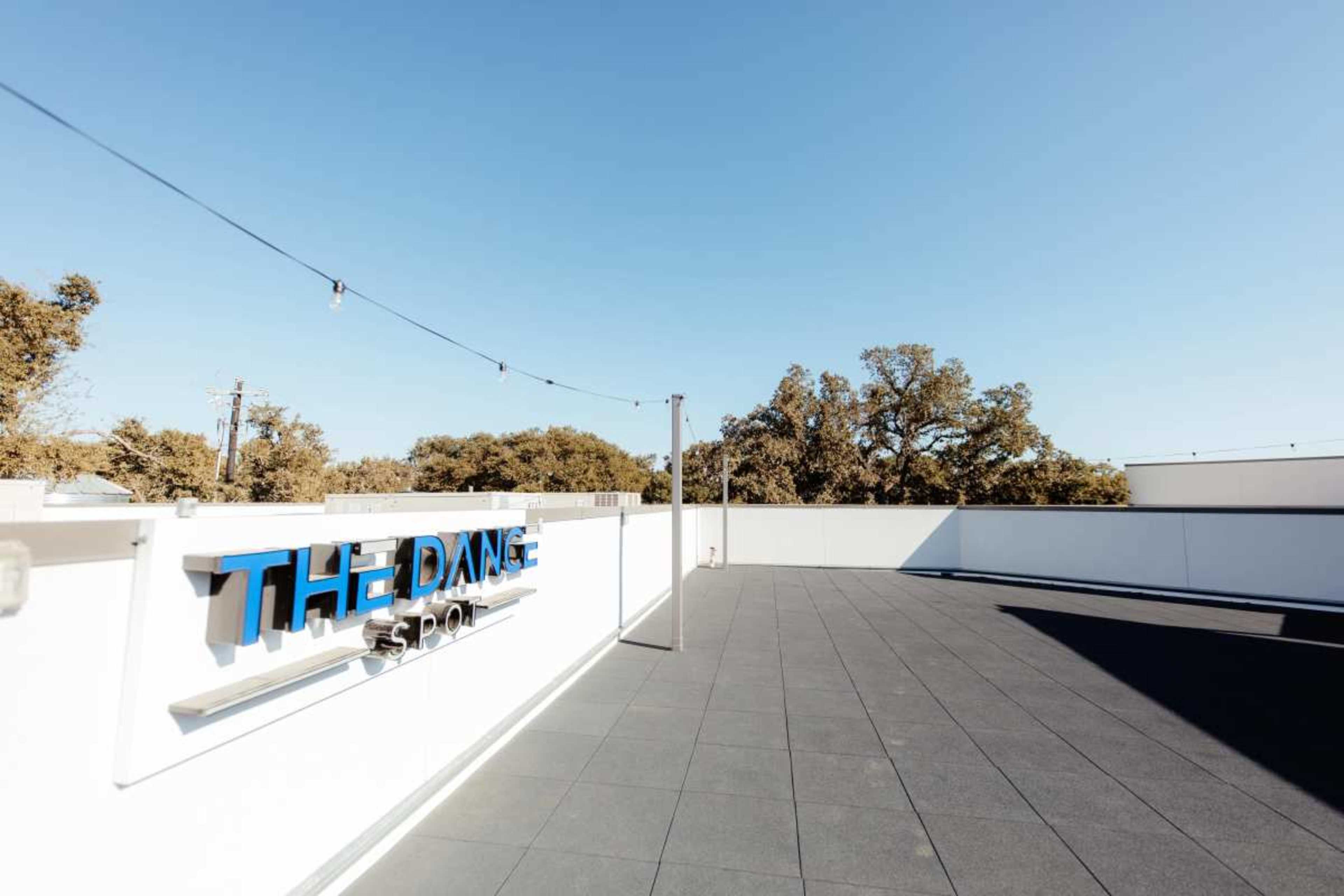 A rooftop space features the sign "THE DANCE SPOT" against a clear blue sky with trees in the background.