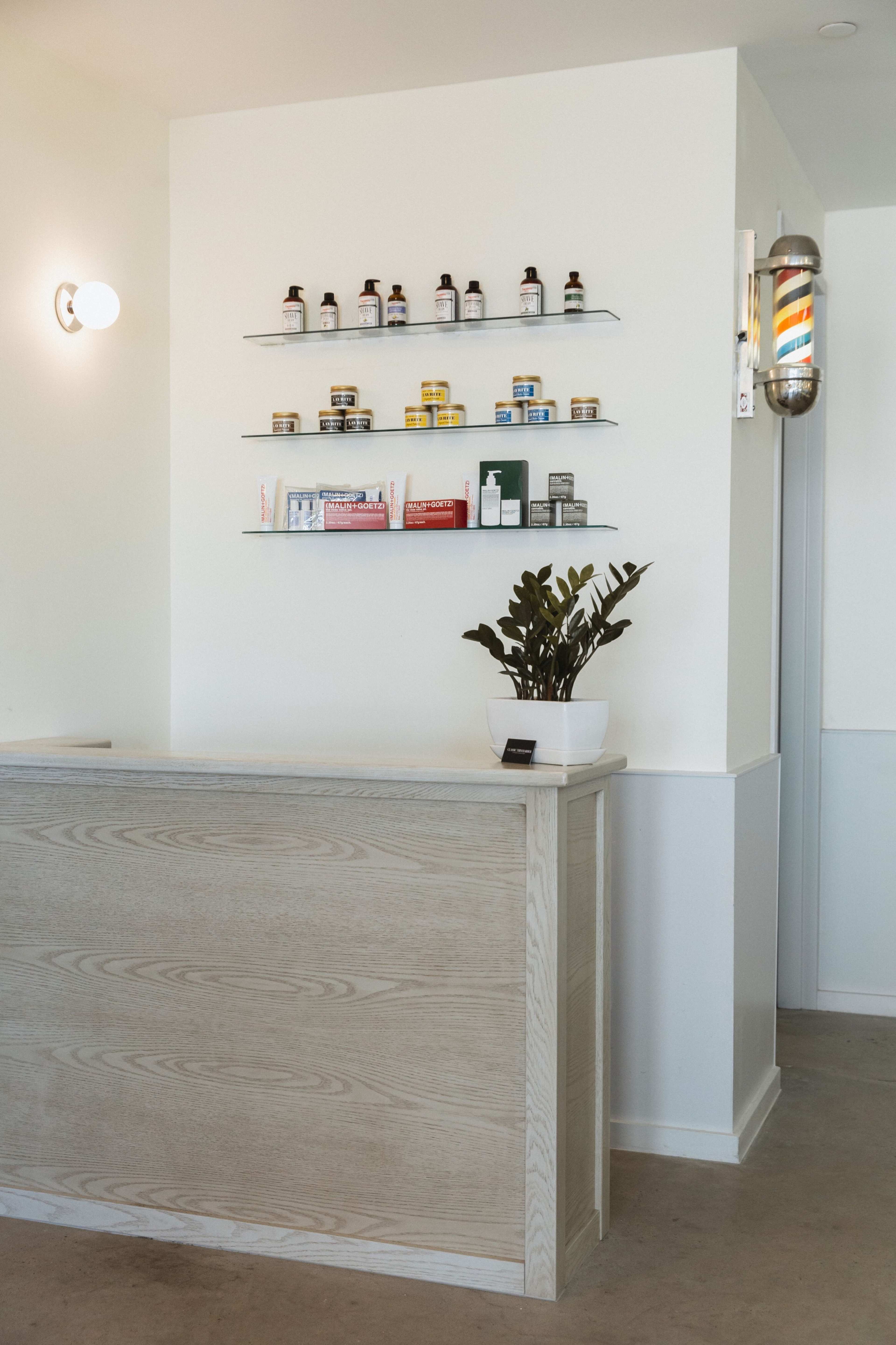A modern reception area with a wooden front desk, shelves displaying various products, and a potted plant.