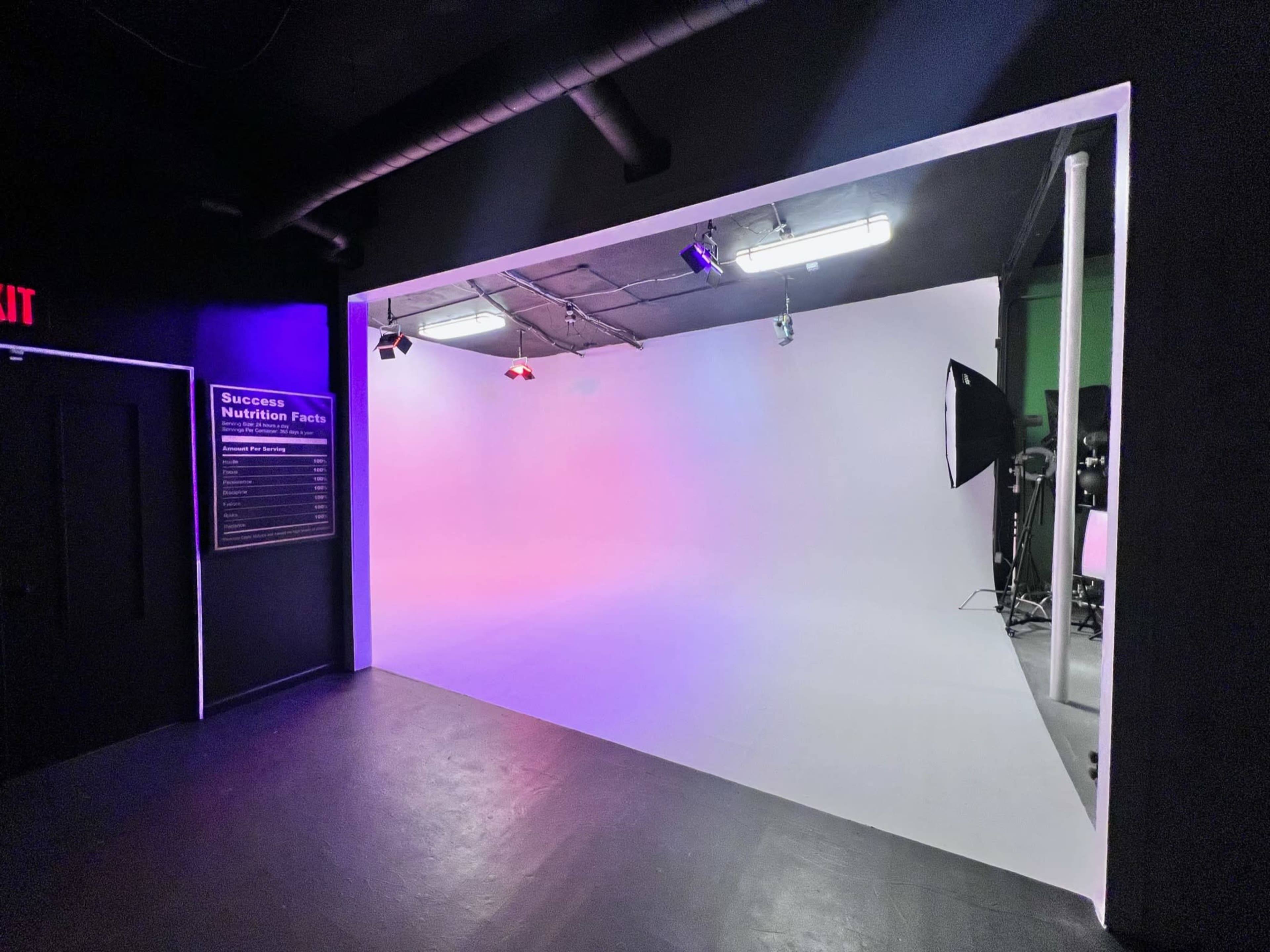A photography studio with a white backdrop, various lights, and a sign on the wall featuring "Success Nutrition Facts."