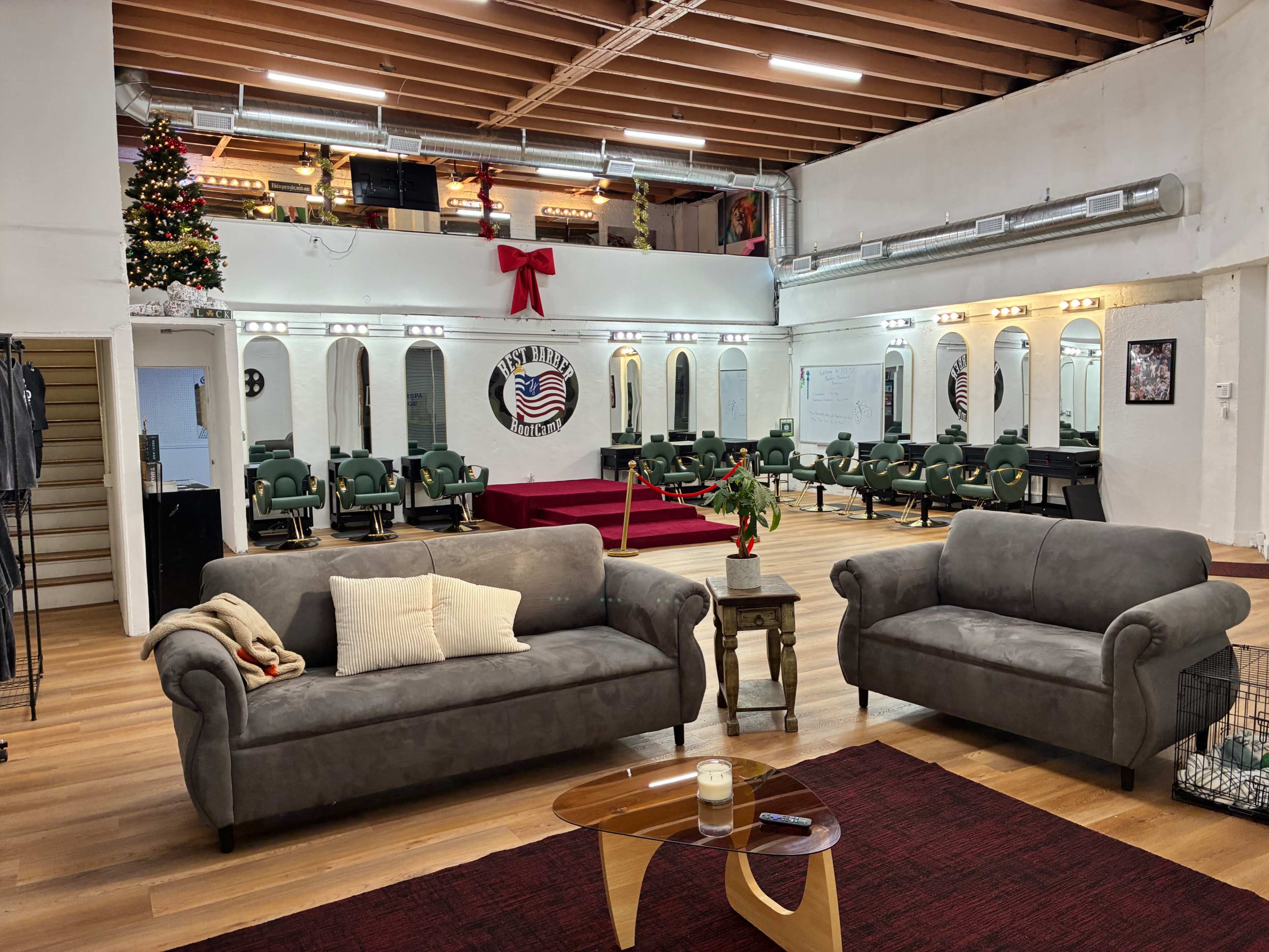 The image shows a spacious barber shop interior with multiple barber chairs, decorative mirrors, and a seating area featuring gray sofas and a coffee table.