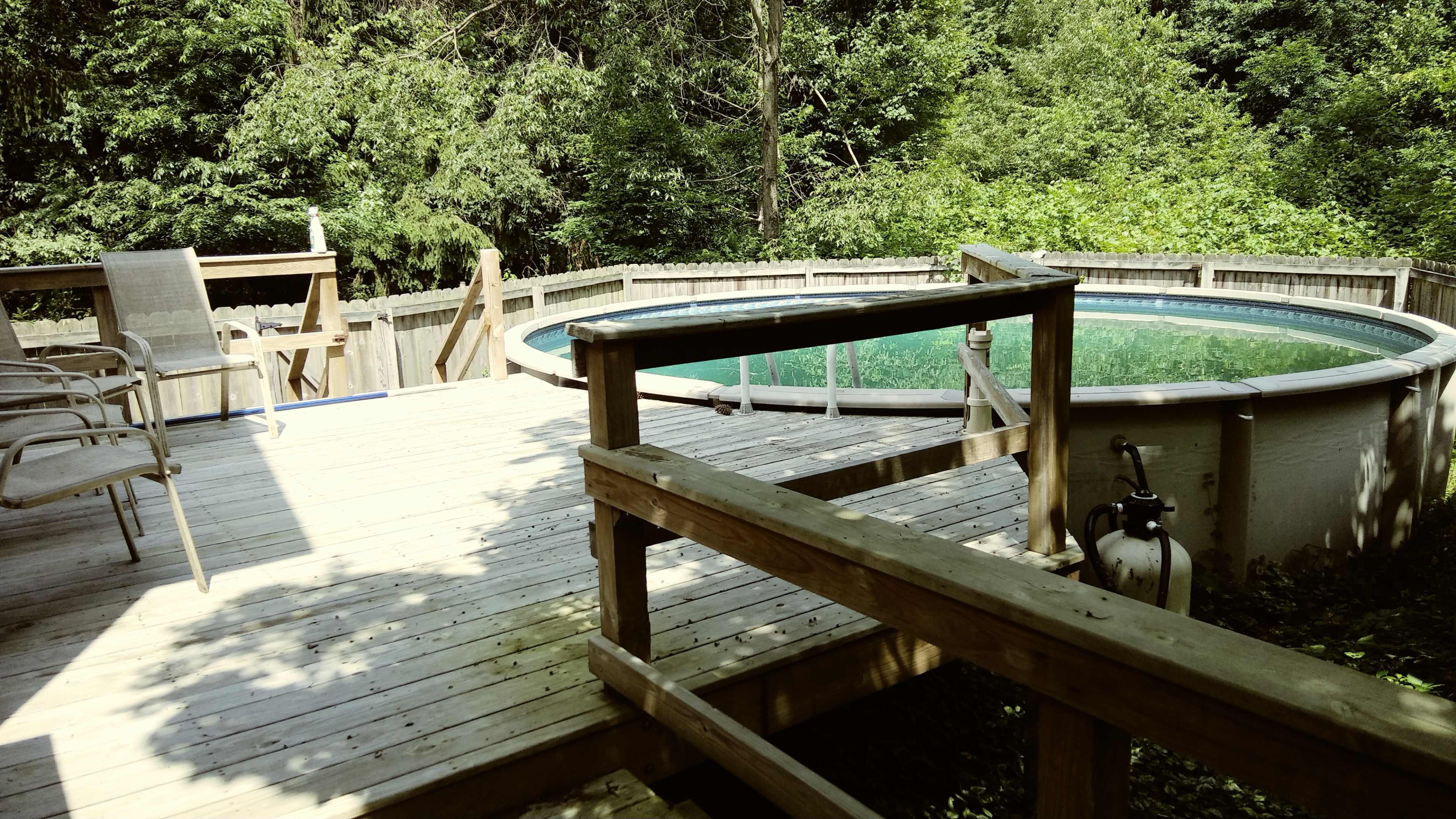 A wooden deck leading to a round above-ground pool surrounded by greenery.