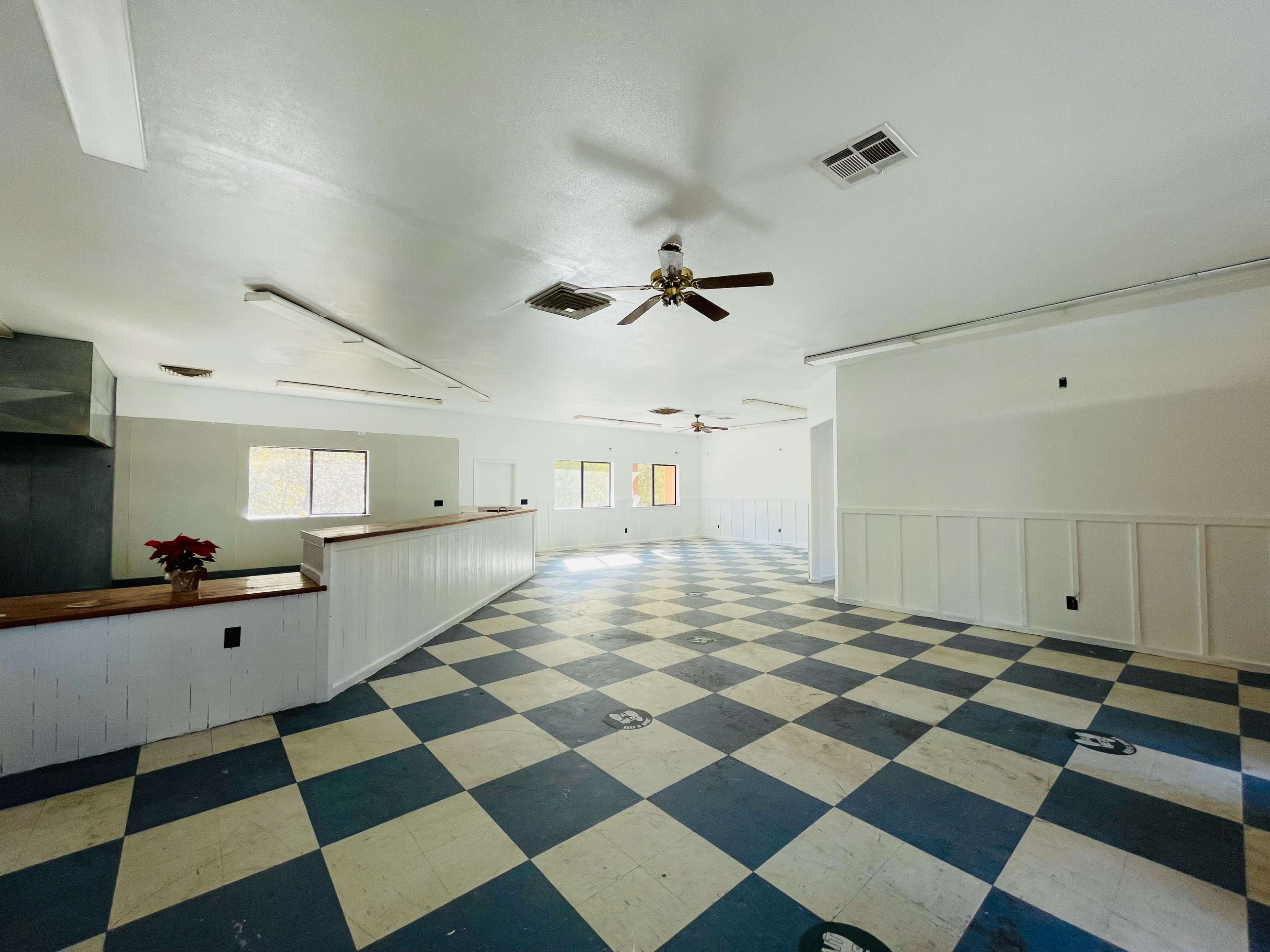An empty room with a checkerboard blue and white floor, ceiling fans, and several windows allowing natural light.