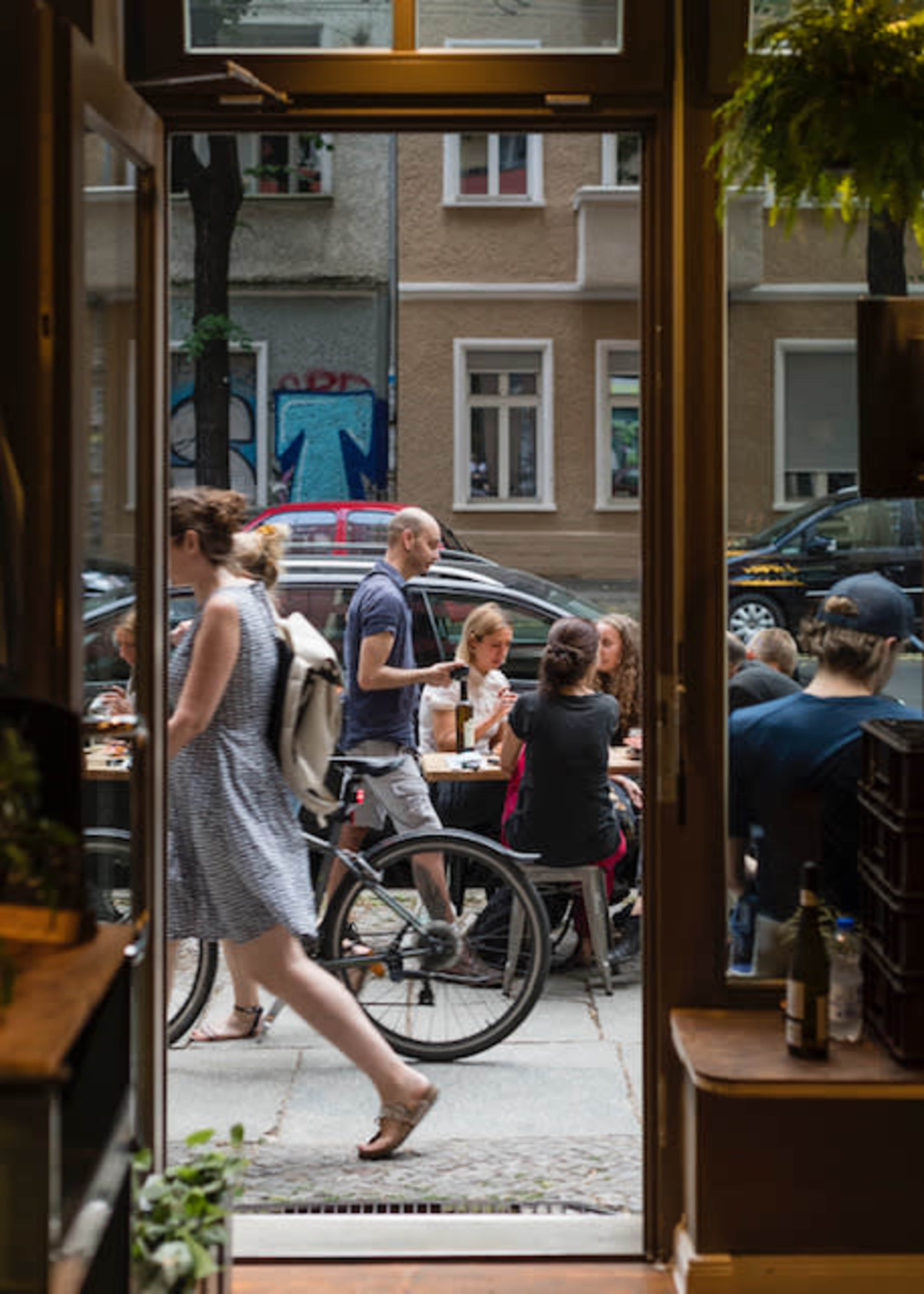 A cyclist passes by as diners sit at outdoor tables near a storefront.