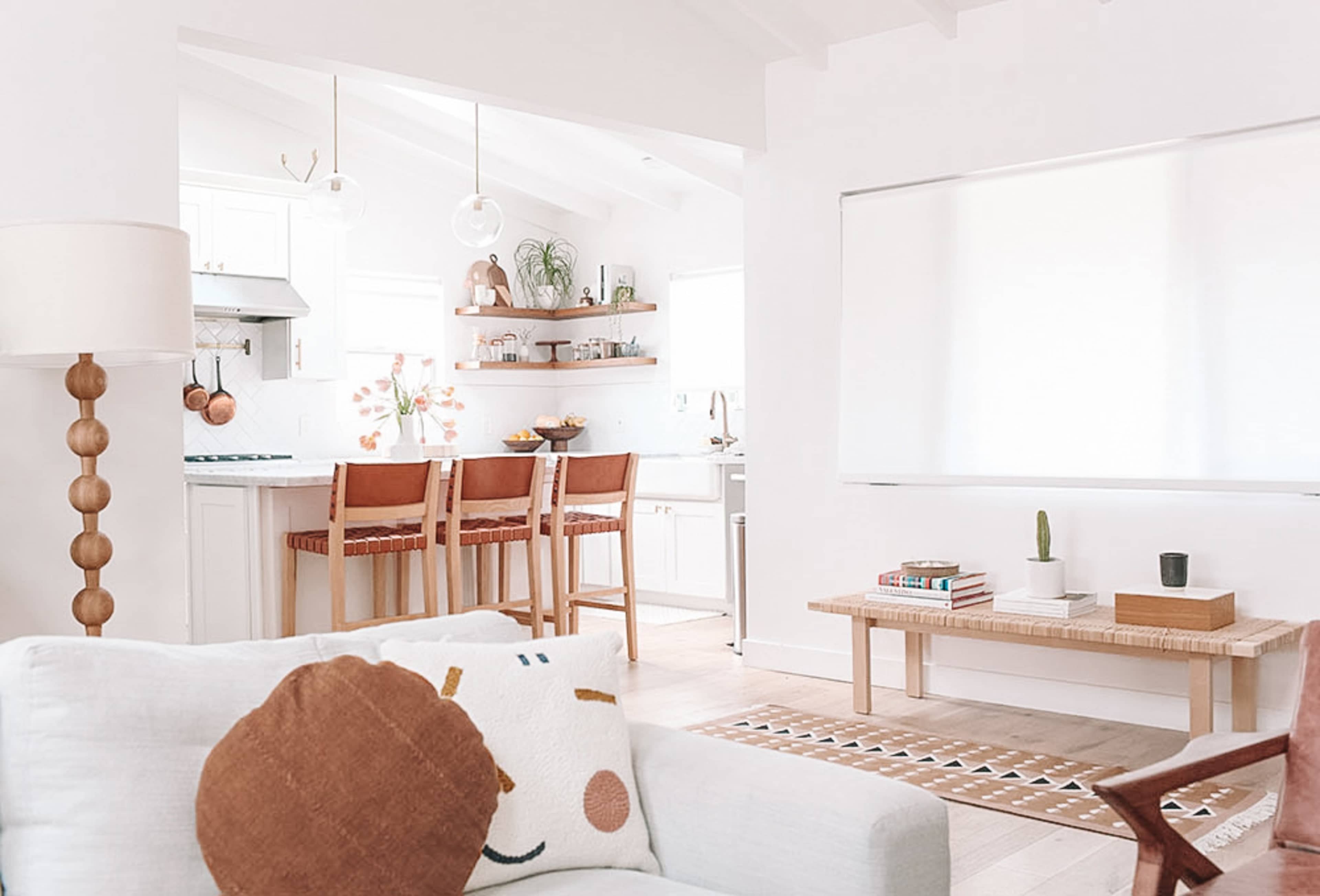 A modern, open-concept living space with a kitchen, dining area, and a small seating area featuring light-colored furniture and wooden accents.