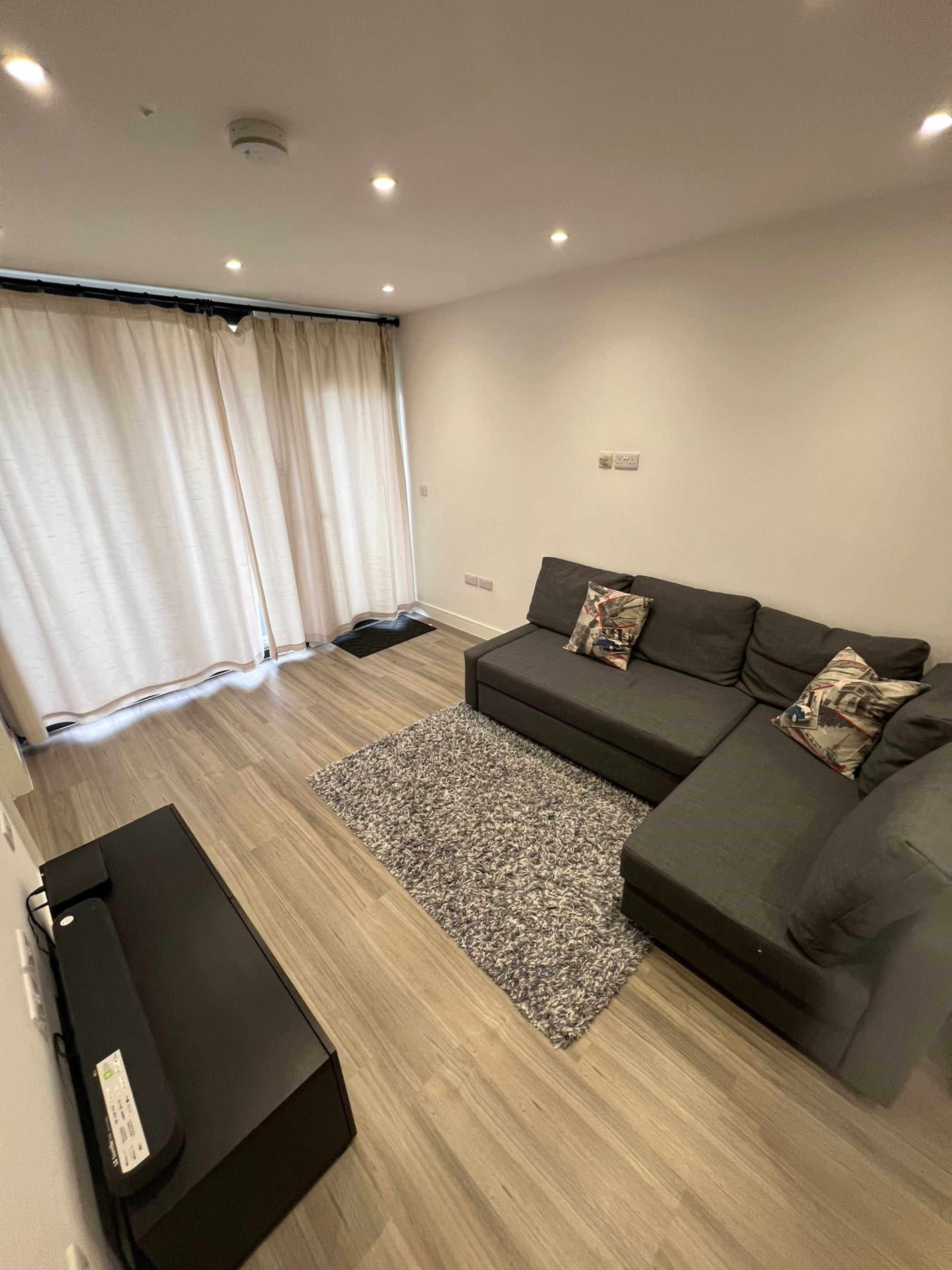 A living room features a grey sectional sofa, a rug, and light-colored curtains covering a window.
