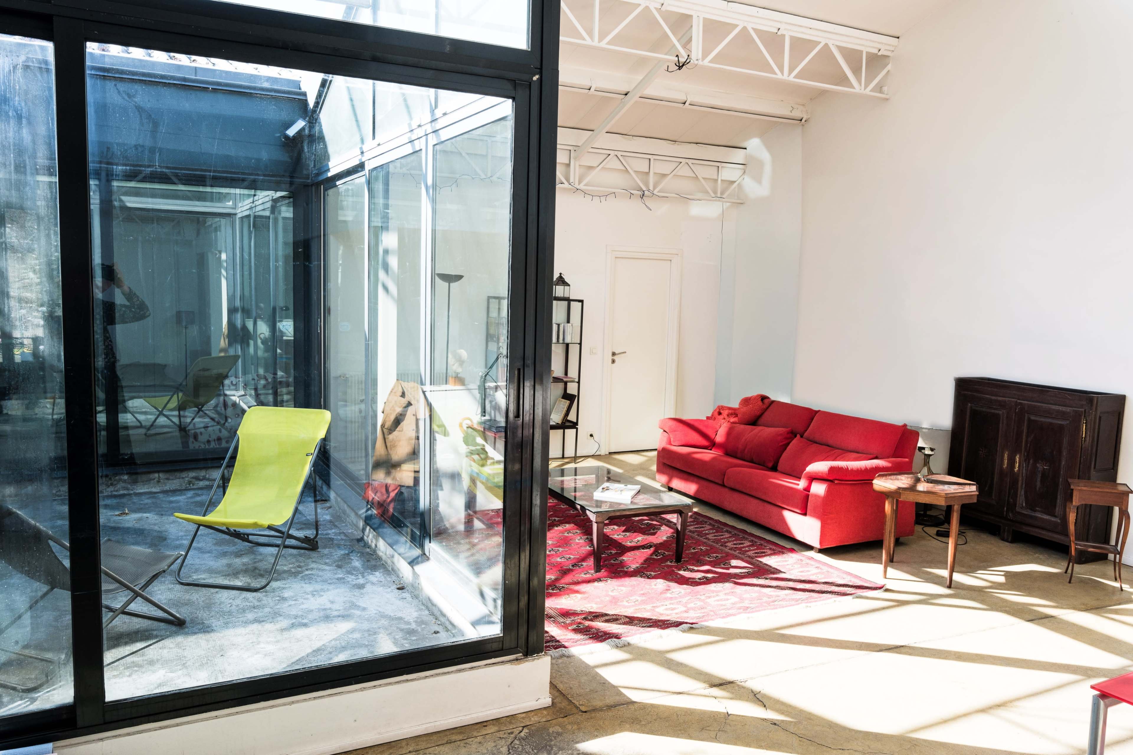 The image shows a bright, modern interior featuring a red sofa, a yellow lounge chair, and large glass windows.