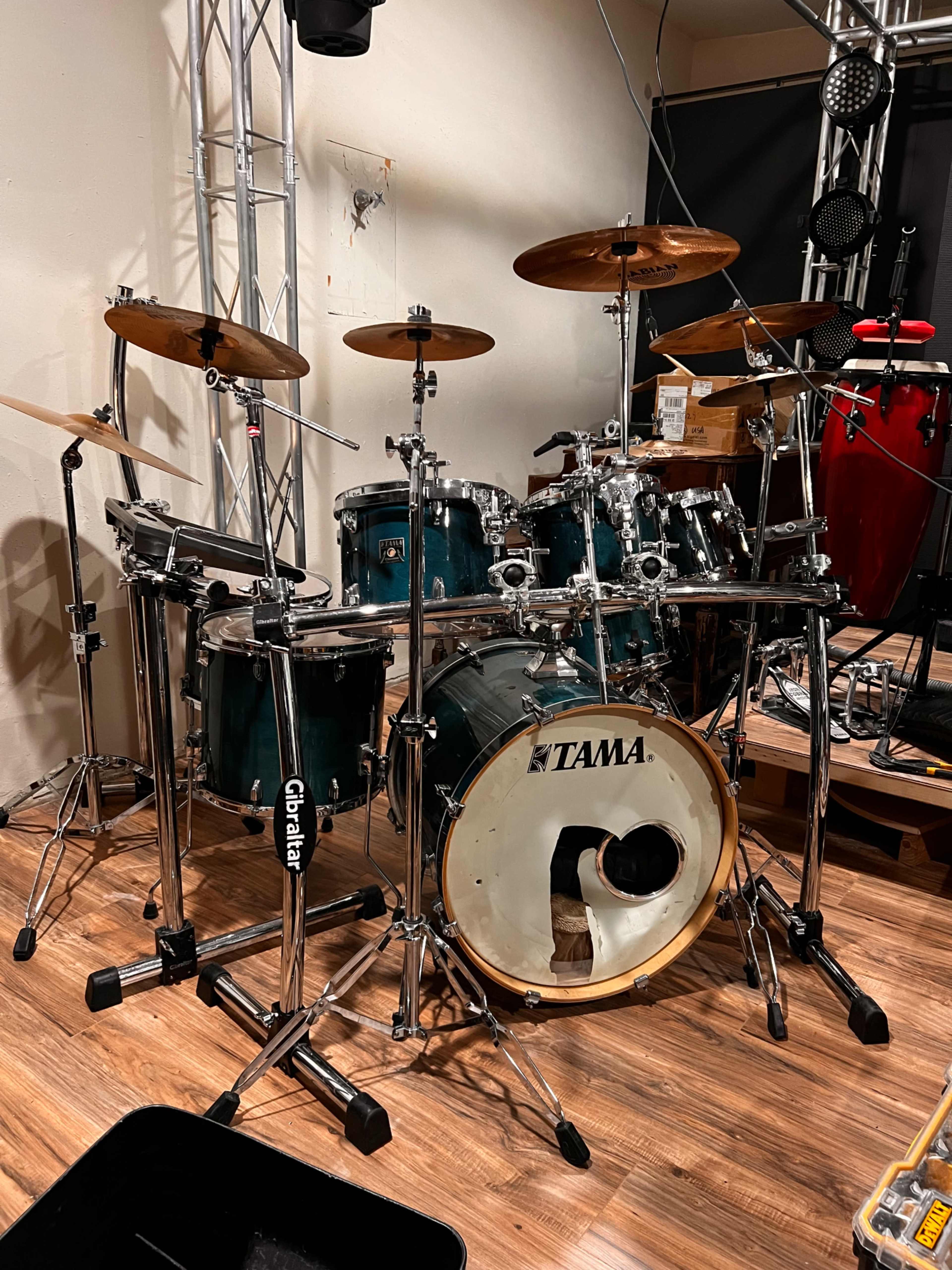 A Tama drum set with multiple cymbals and stands is positioned on a wooden floor in a studio environment.