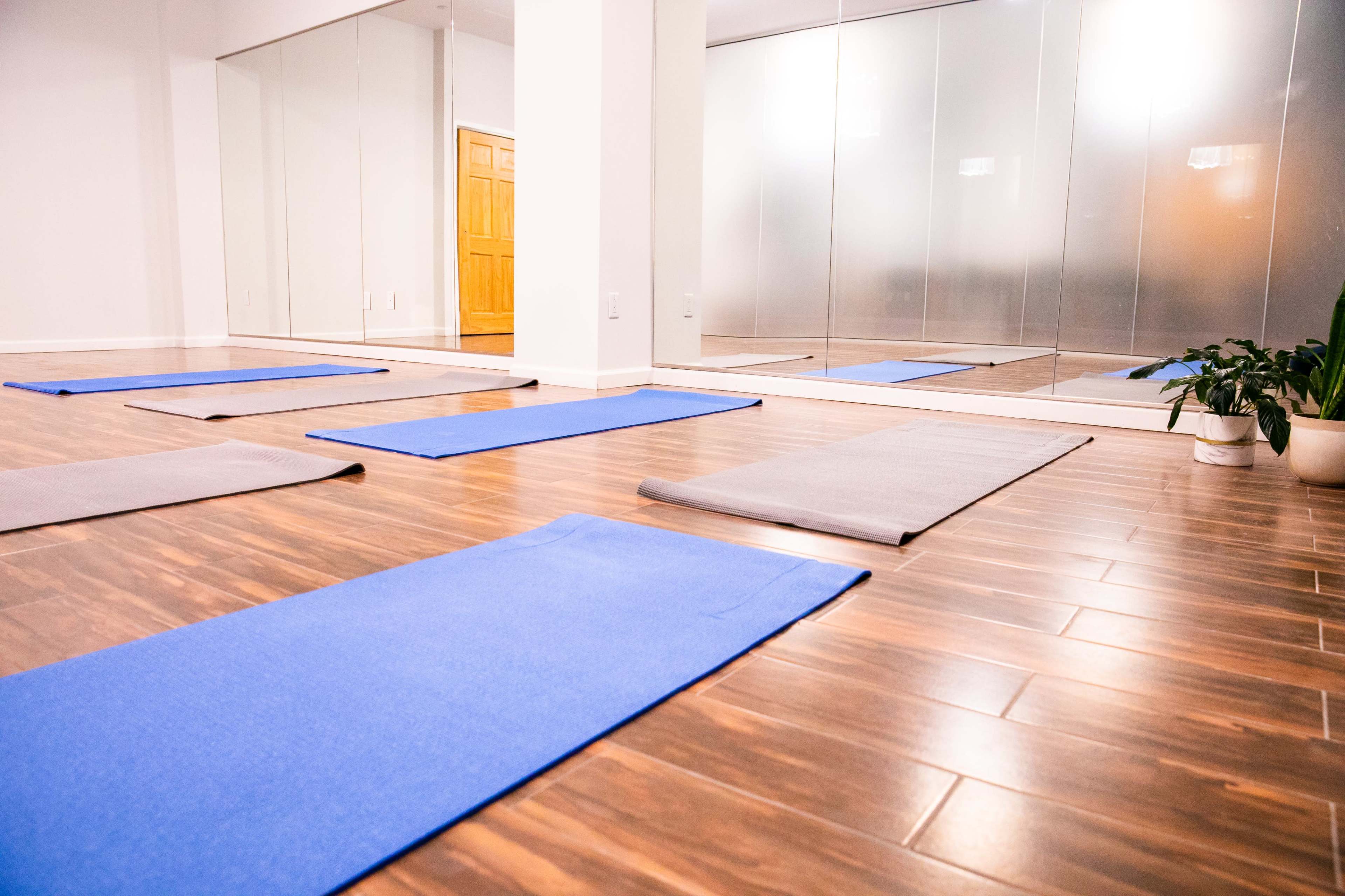 An empty yoga studio with blue mats arranged on a wooden floor and mirrors reflecting the space.