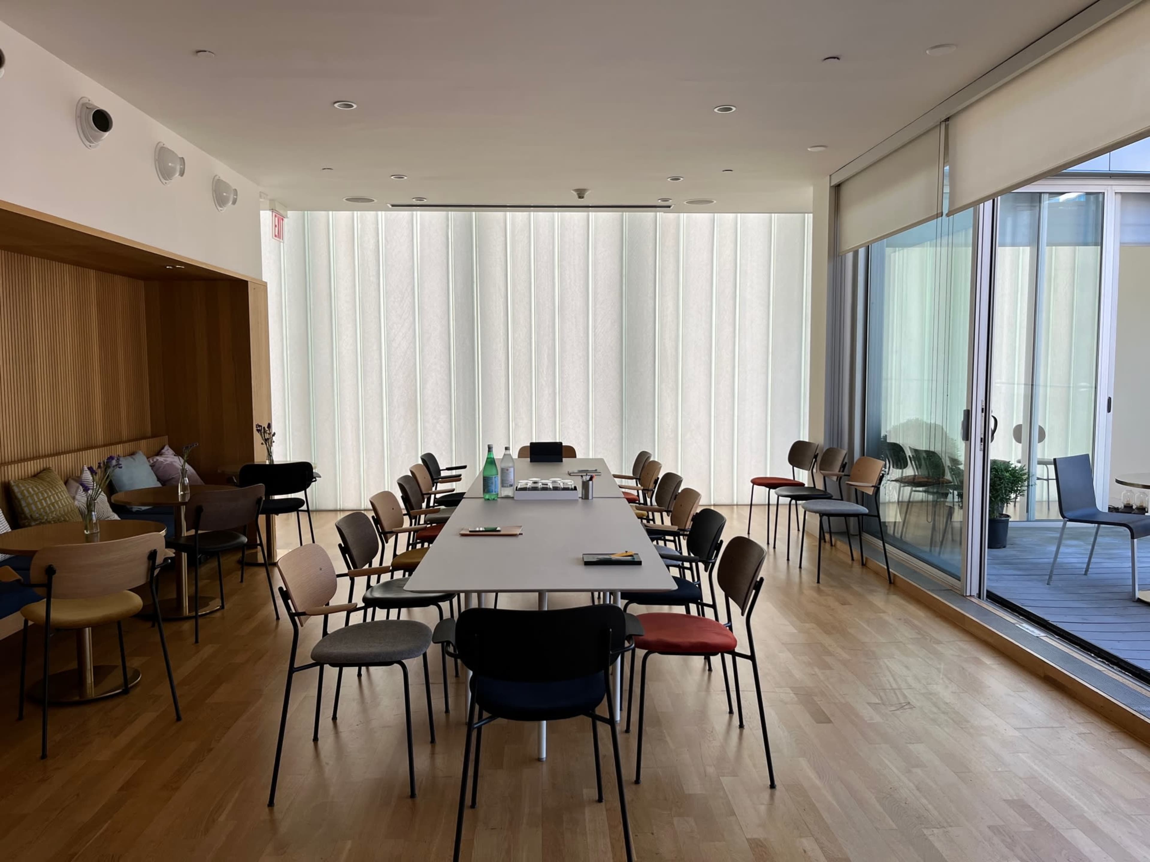 A meeting room features a long table surrounded by chairs and large windows allowing natural light to enter.