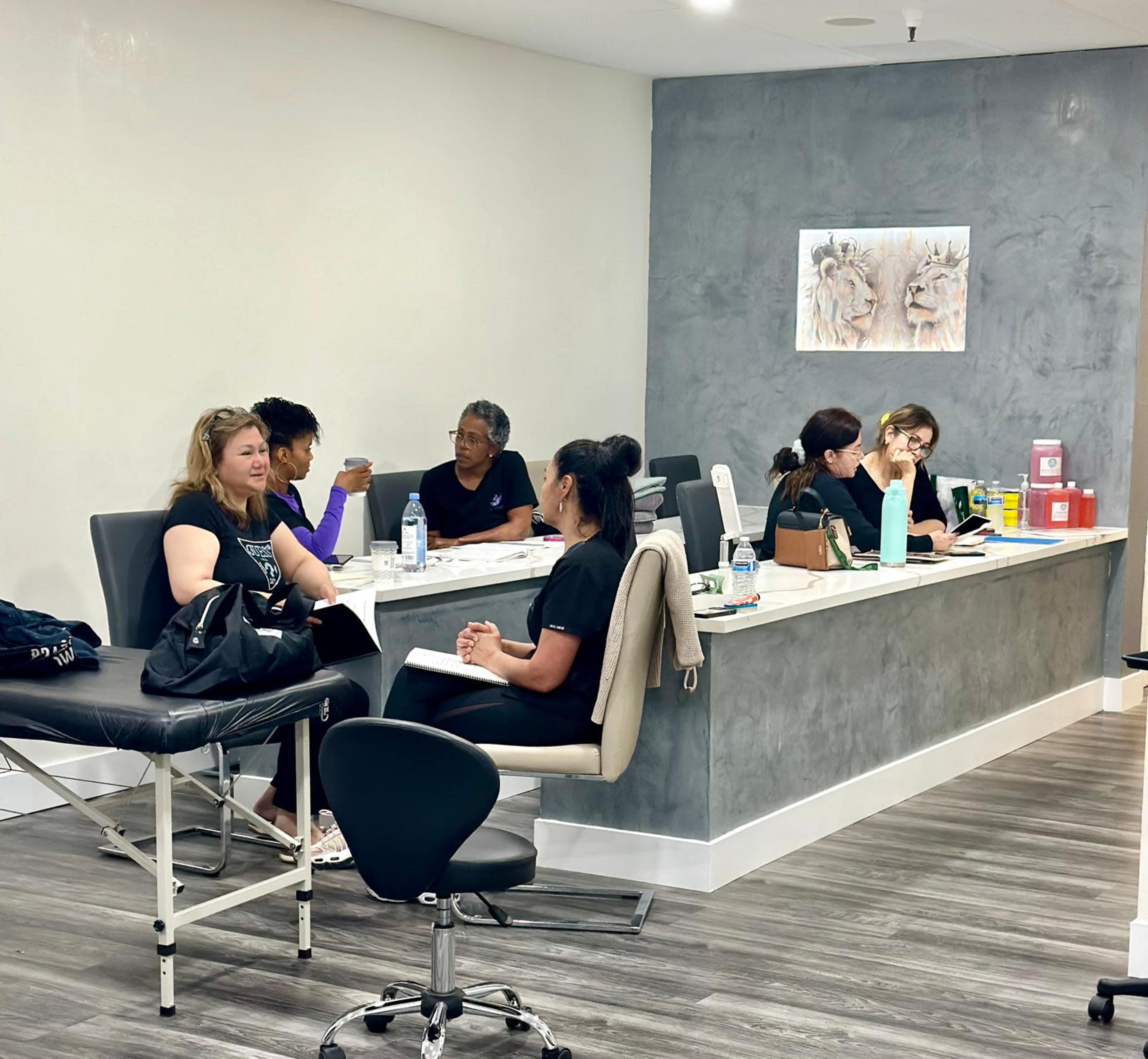 The image shows a modern spa or wellness center with several people engaged in conversation and consultation at a reception desk and treatment area.