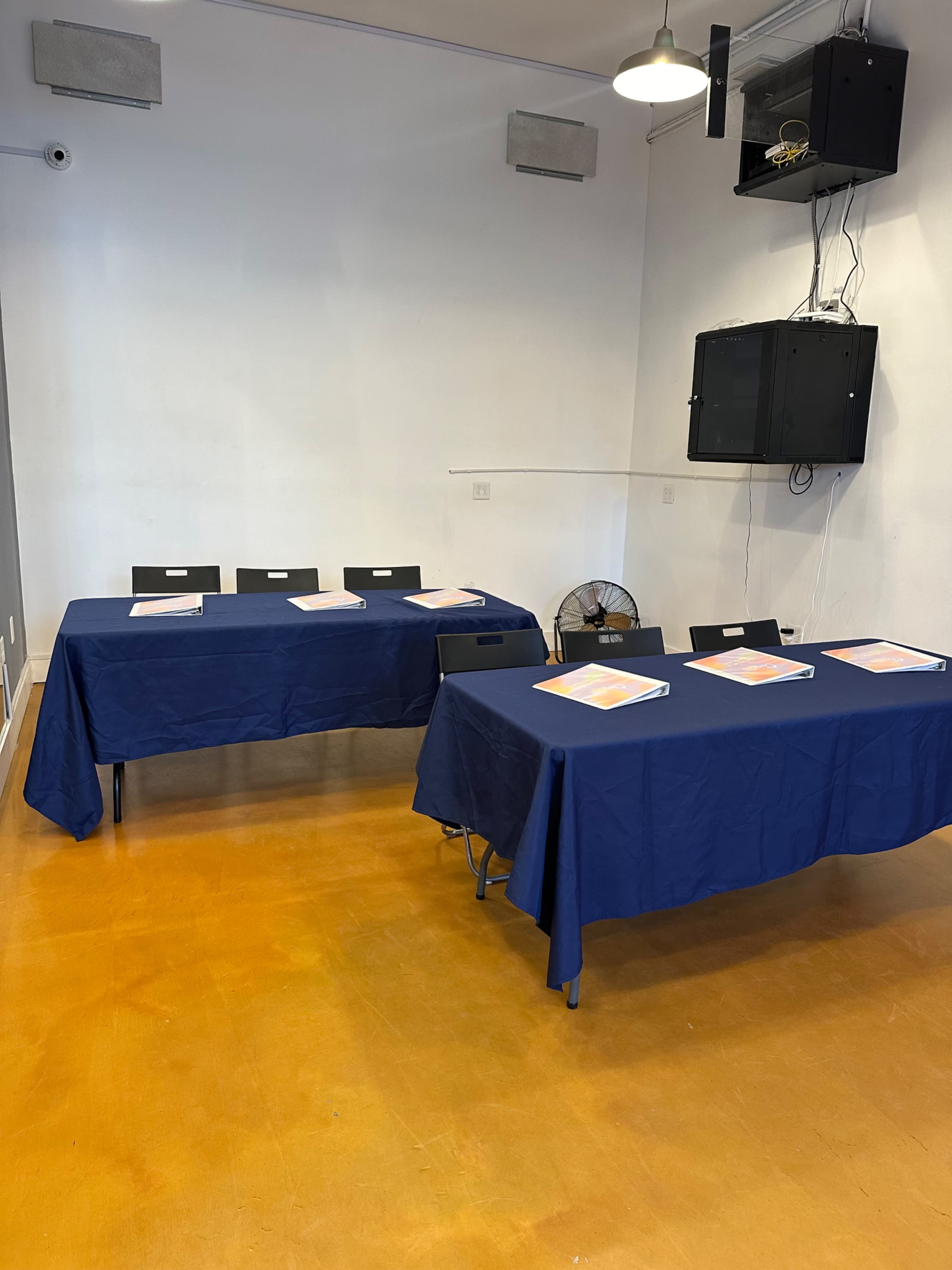 The image shows two tables covered with navy blue tablecloths, each set with several binders, in a well-lit room with a simple, clean design.