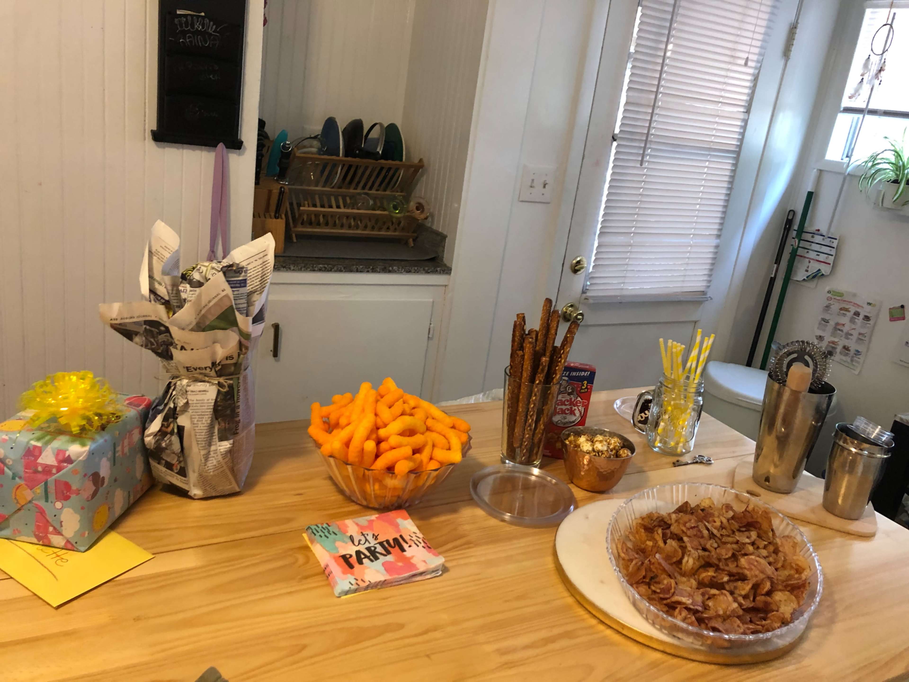 A table is set up with snacks including cheese puffs, pretzels, popcorn, and a tray of bacon, alongside wrapped gifts and a festive card.