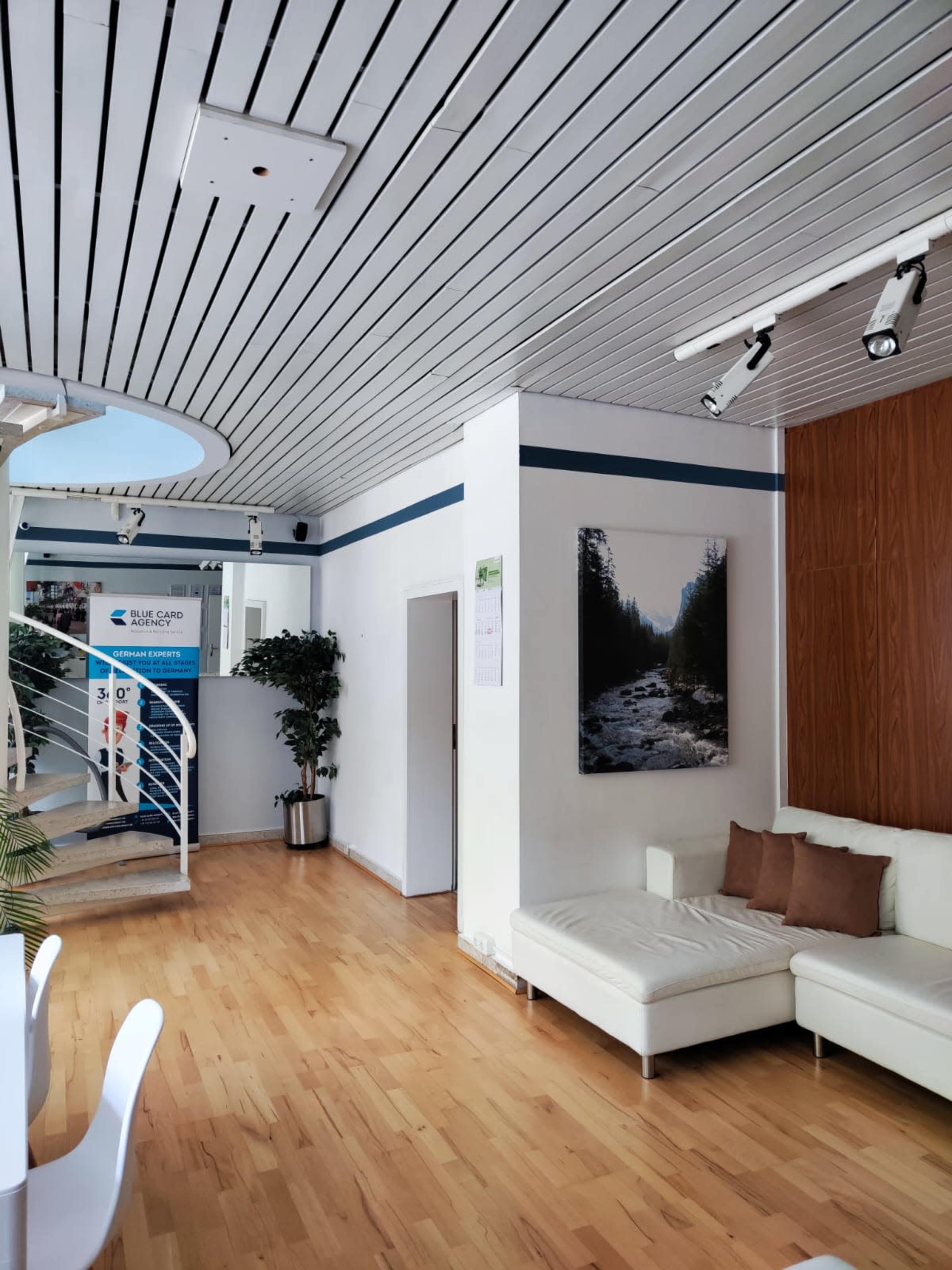 A modern interior space with a spiral staircase, a white sofa, wooden flooring, and a large framed picture on the wall.