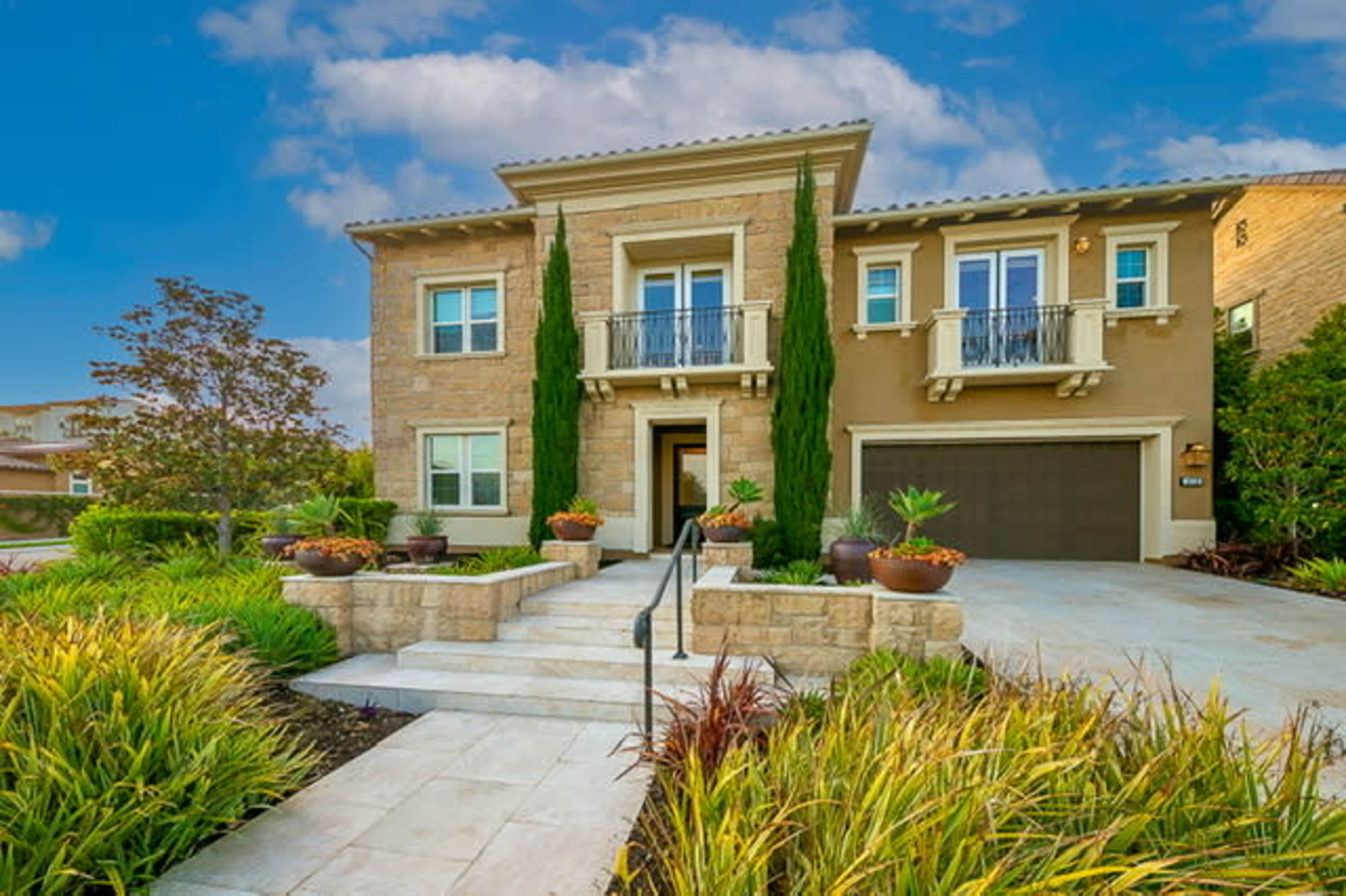 A modern, two-story house with a stone facade, large windows, and landscaped gardens featuring potted plants and neatly arranged greenery.