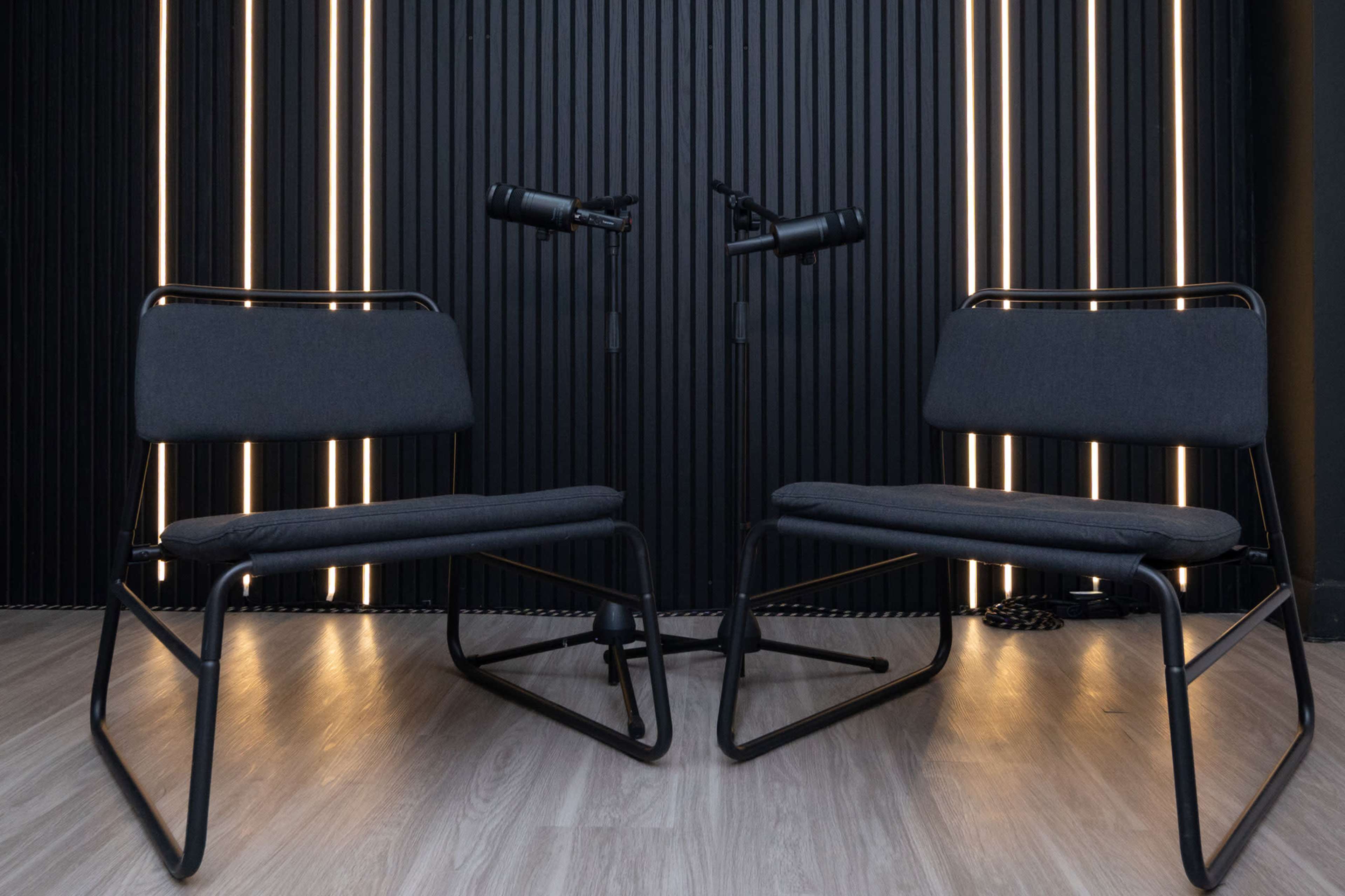 Two black chairs are positioned facing each other in front of a wall with vertical light strips.