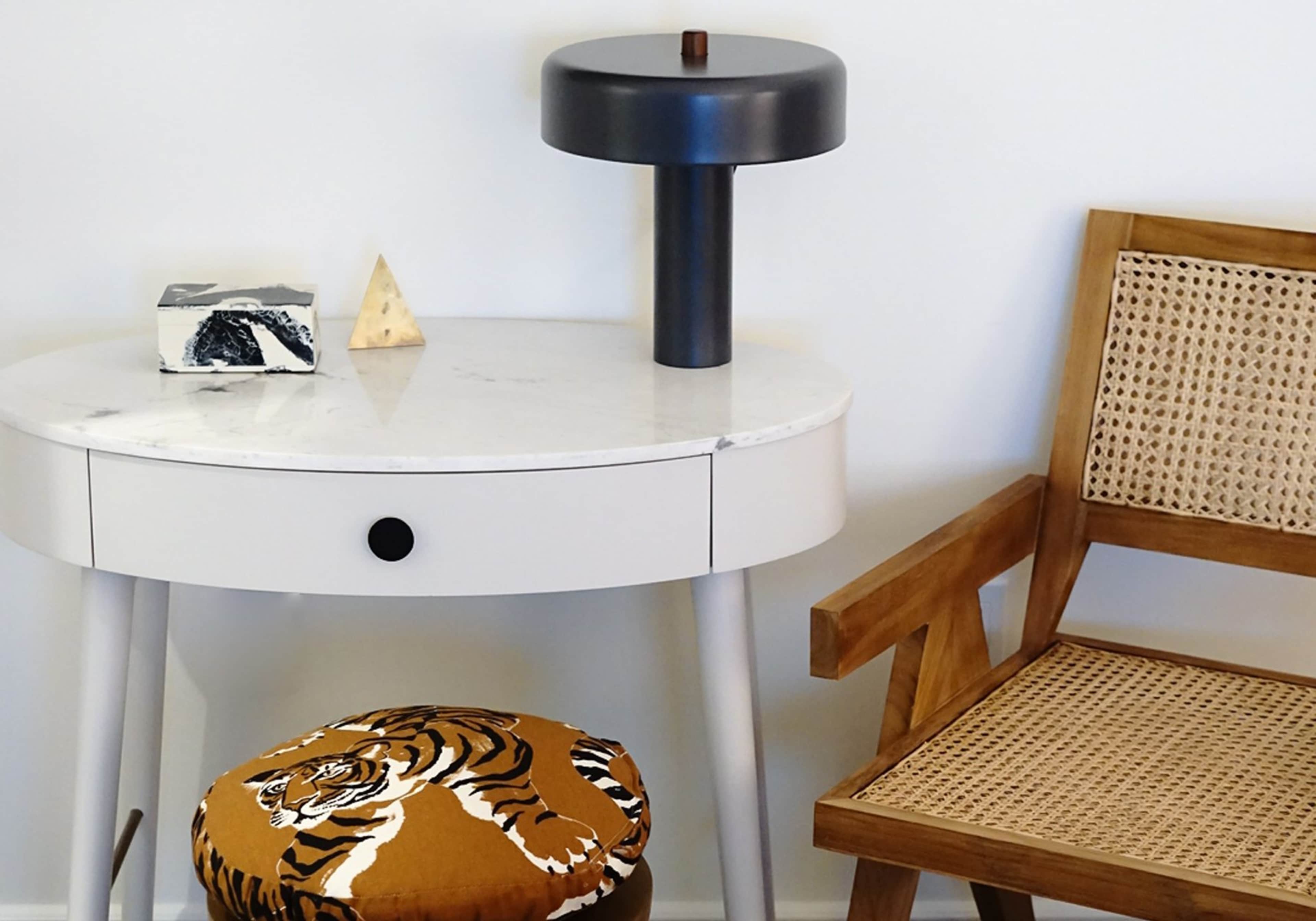 A modern side table with a marble top and a black lamp stands next to a wooden chair and a patterned orange cushion featuring a tiger design.