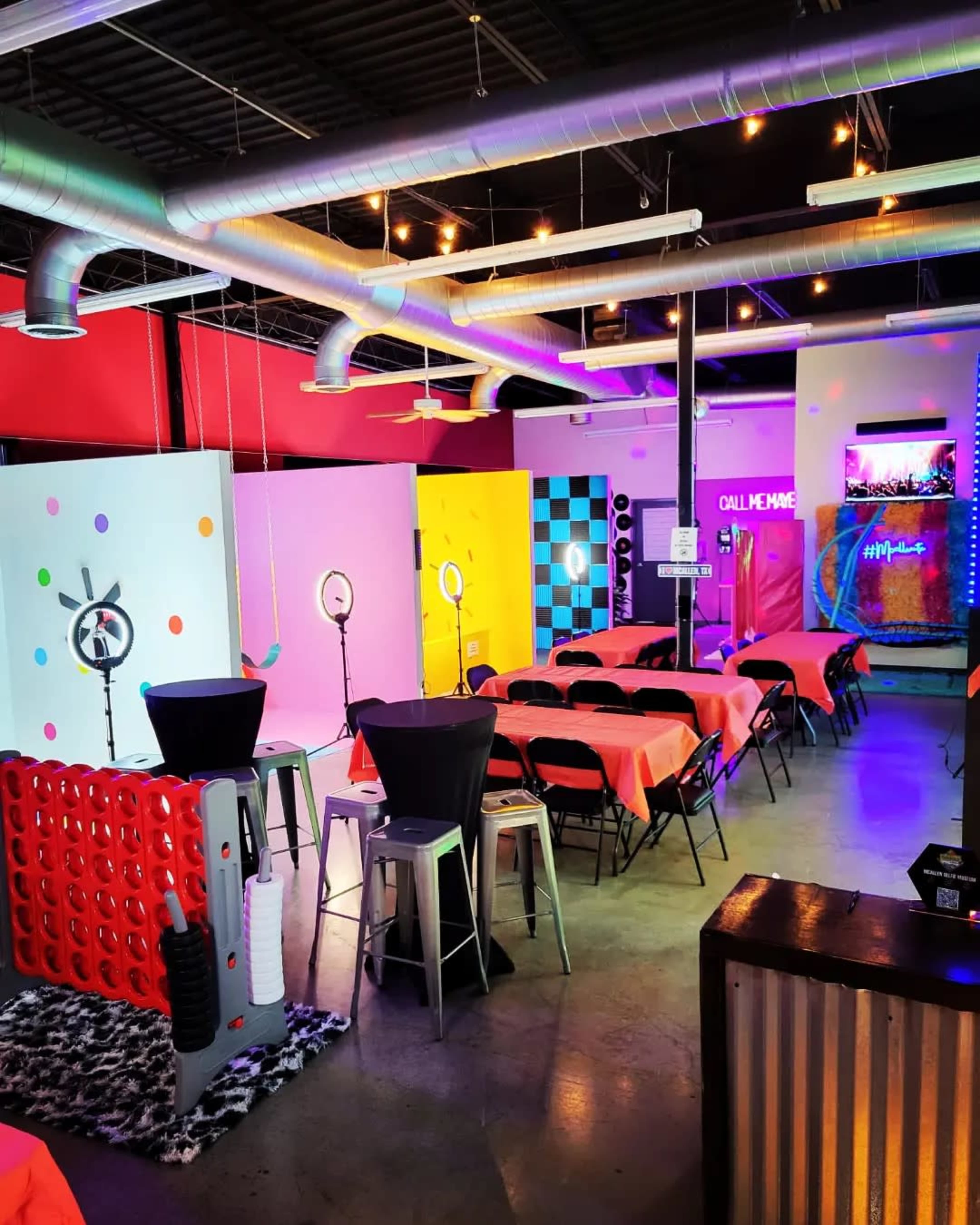 A brightly colored event space with tables covered in orange cloth, decorative walls, and various photo booth setups.