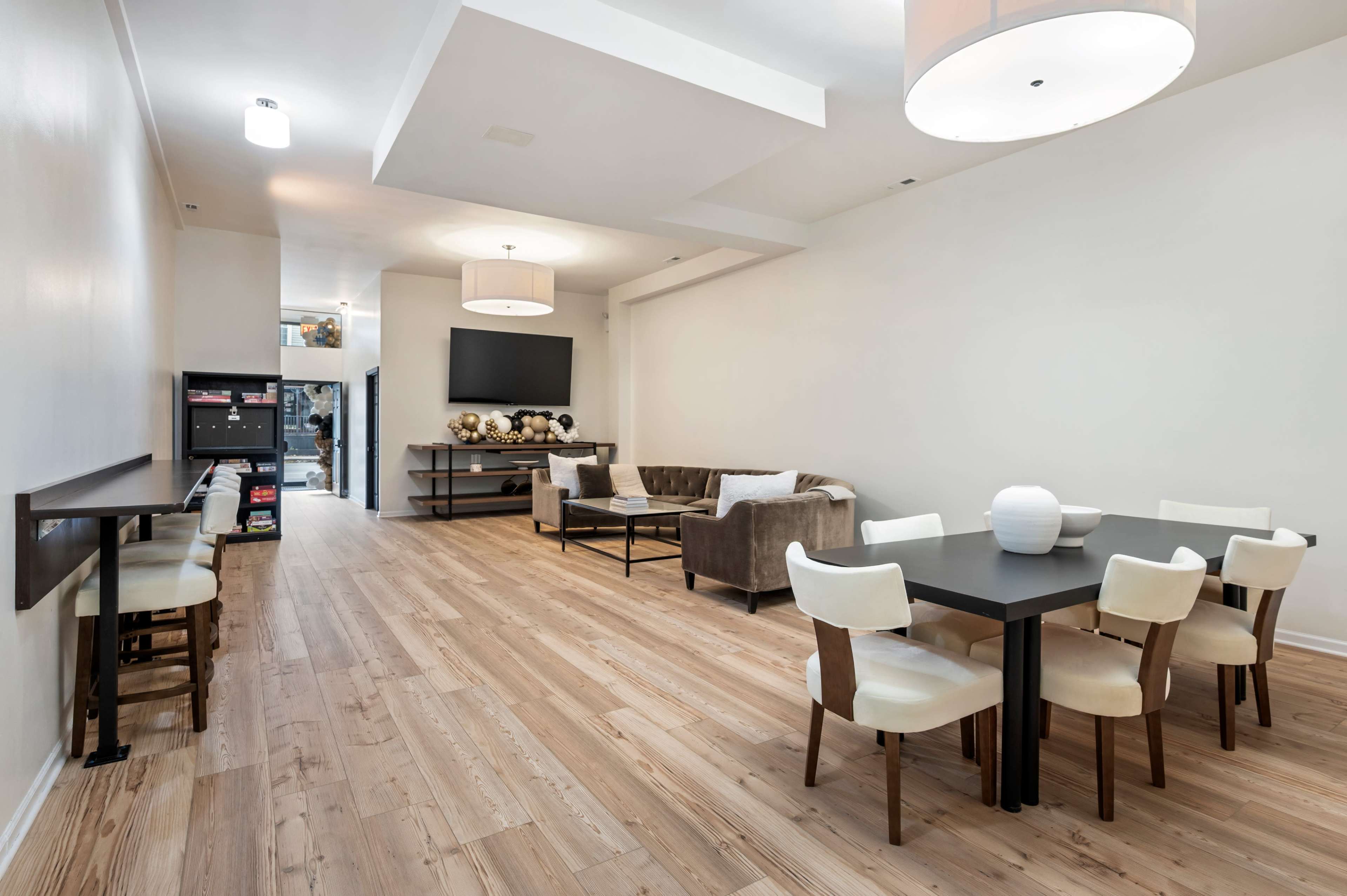 The image shows a modern, open-plan interior with light wood flooring, a seating area featuring a sofa and side chairs, along with a dining table surrounded by white chairs.