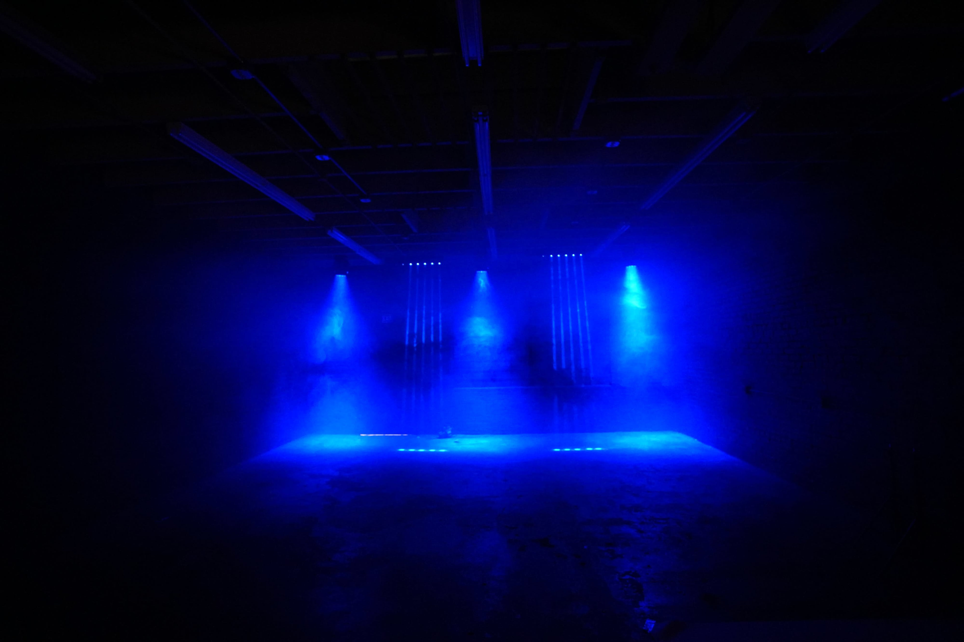 The image shows a dimly lit space with blue spotlights shining through a foggy atmosphere.