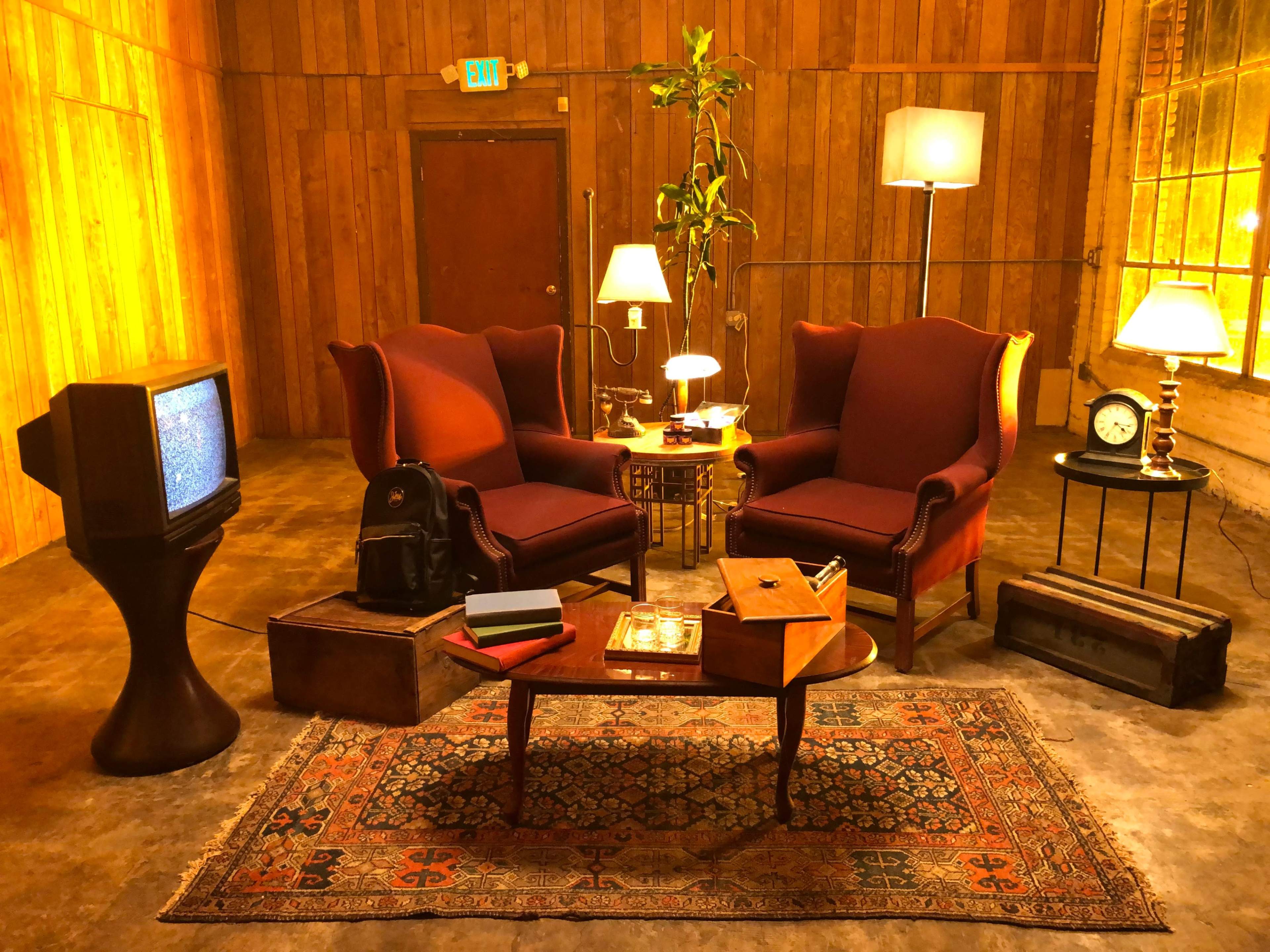The scene features a vintage-style living room with two red armchairs, a wooden table, an old television, and various decorative items under warm lighting.