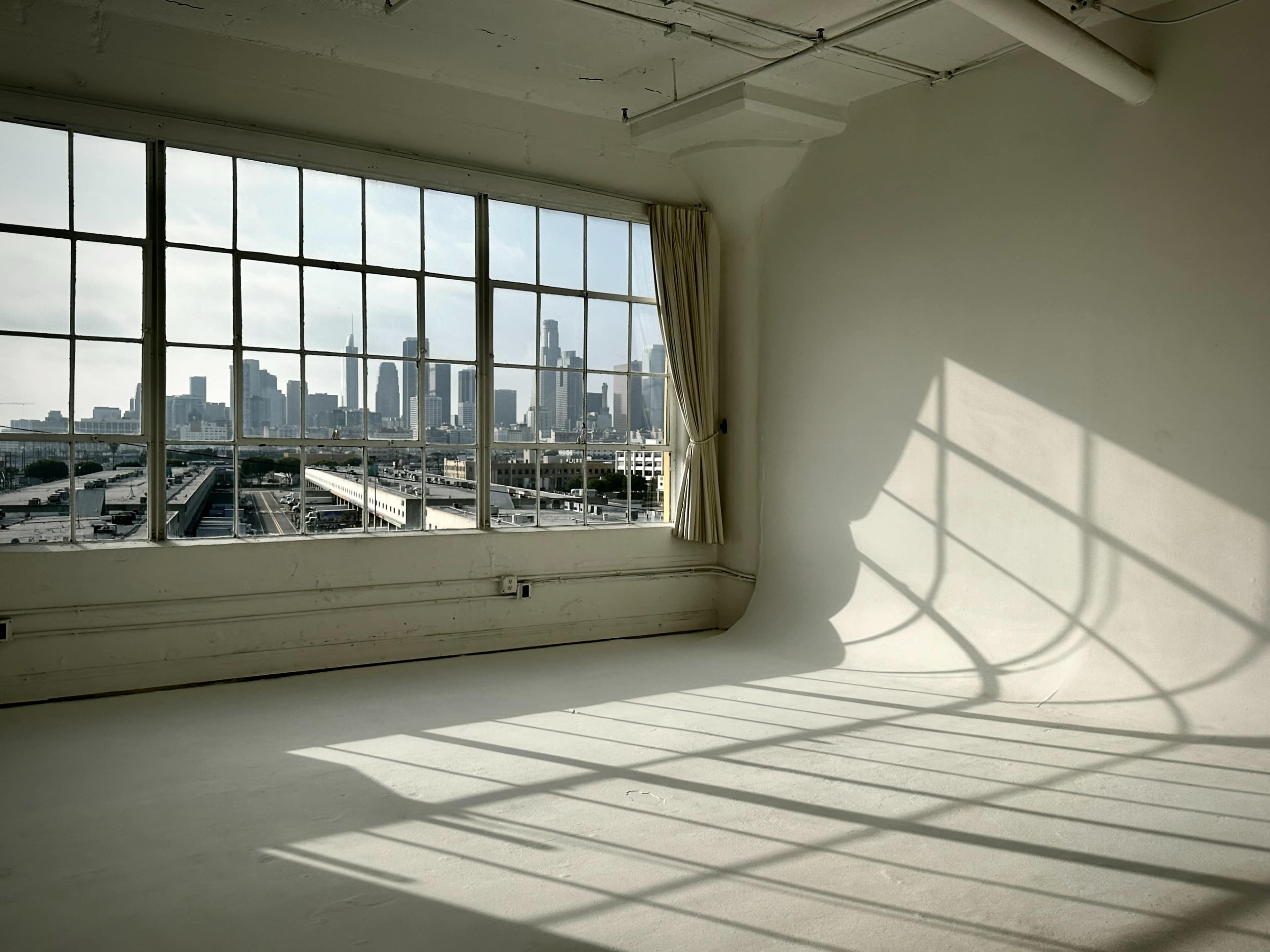 A large window offers a view of a city skyline, casting shadows onto the empty floor of a sunlit room.