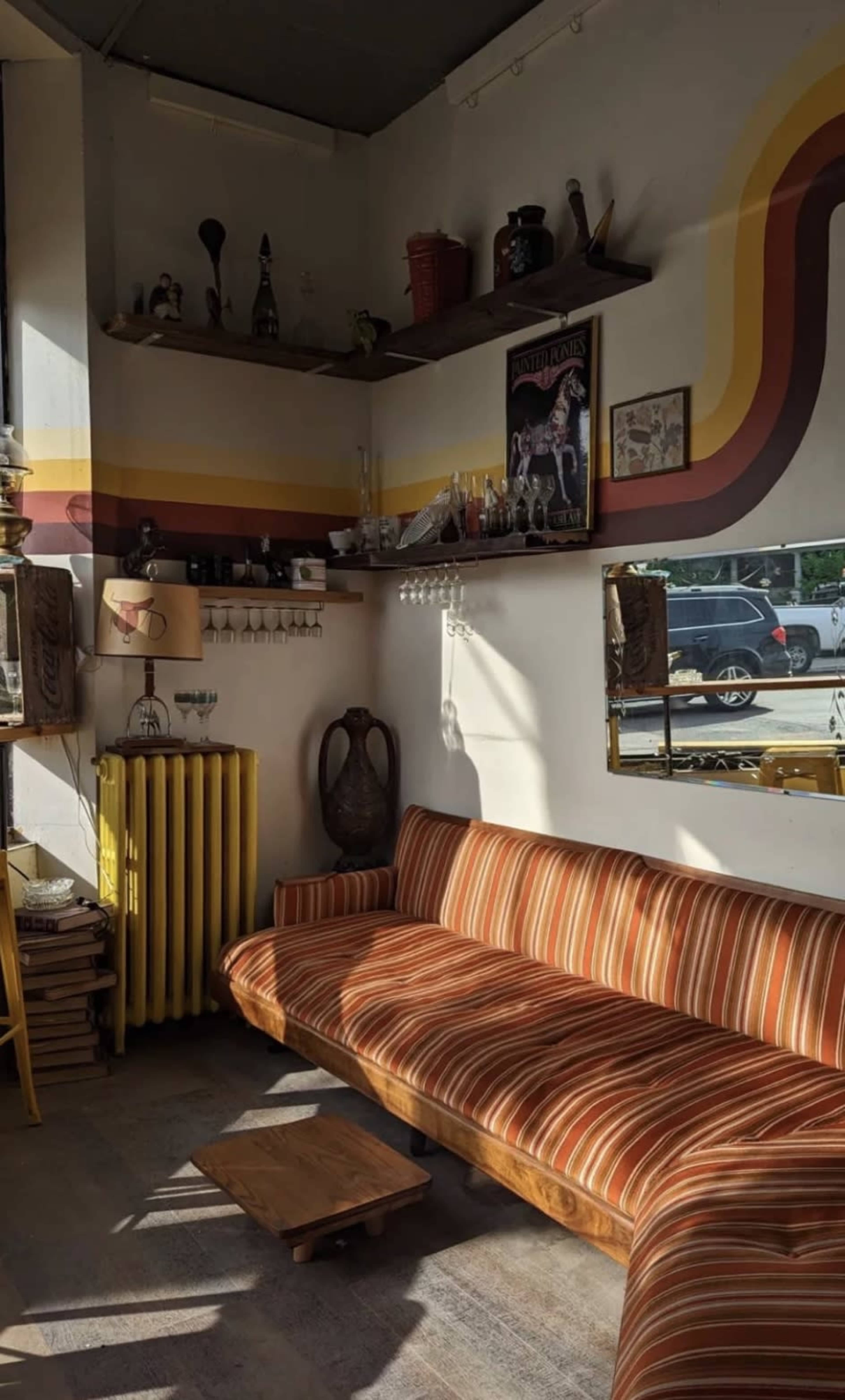 A striped sofa sits in a sunlit corner of a room adorned with shelves displaying various decor items.