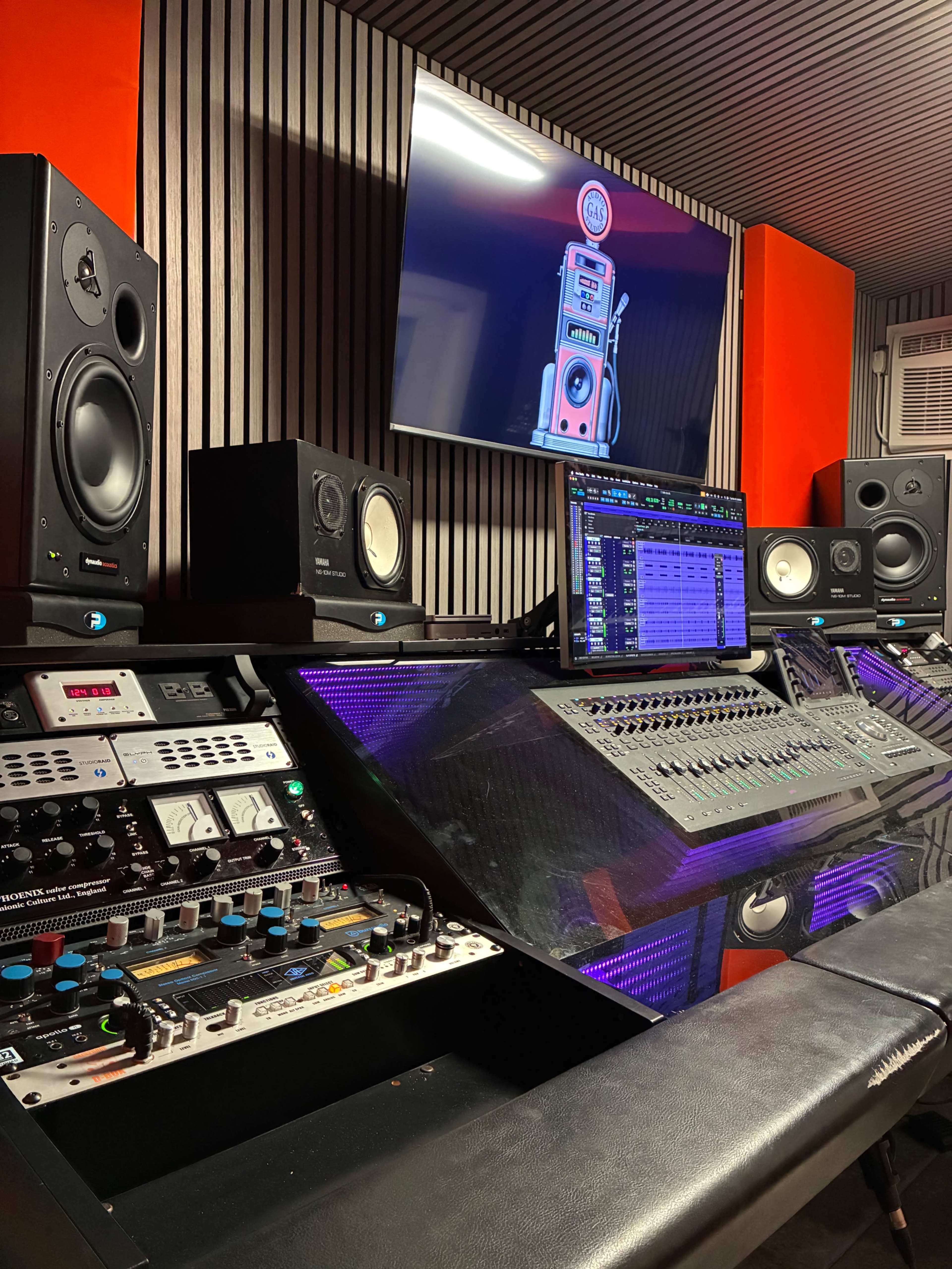 The image shows a modern audio recording studio with a mix console, studio monitors, and a computer screen displaying audio software.