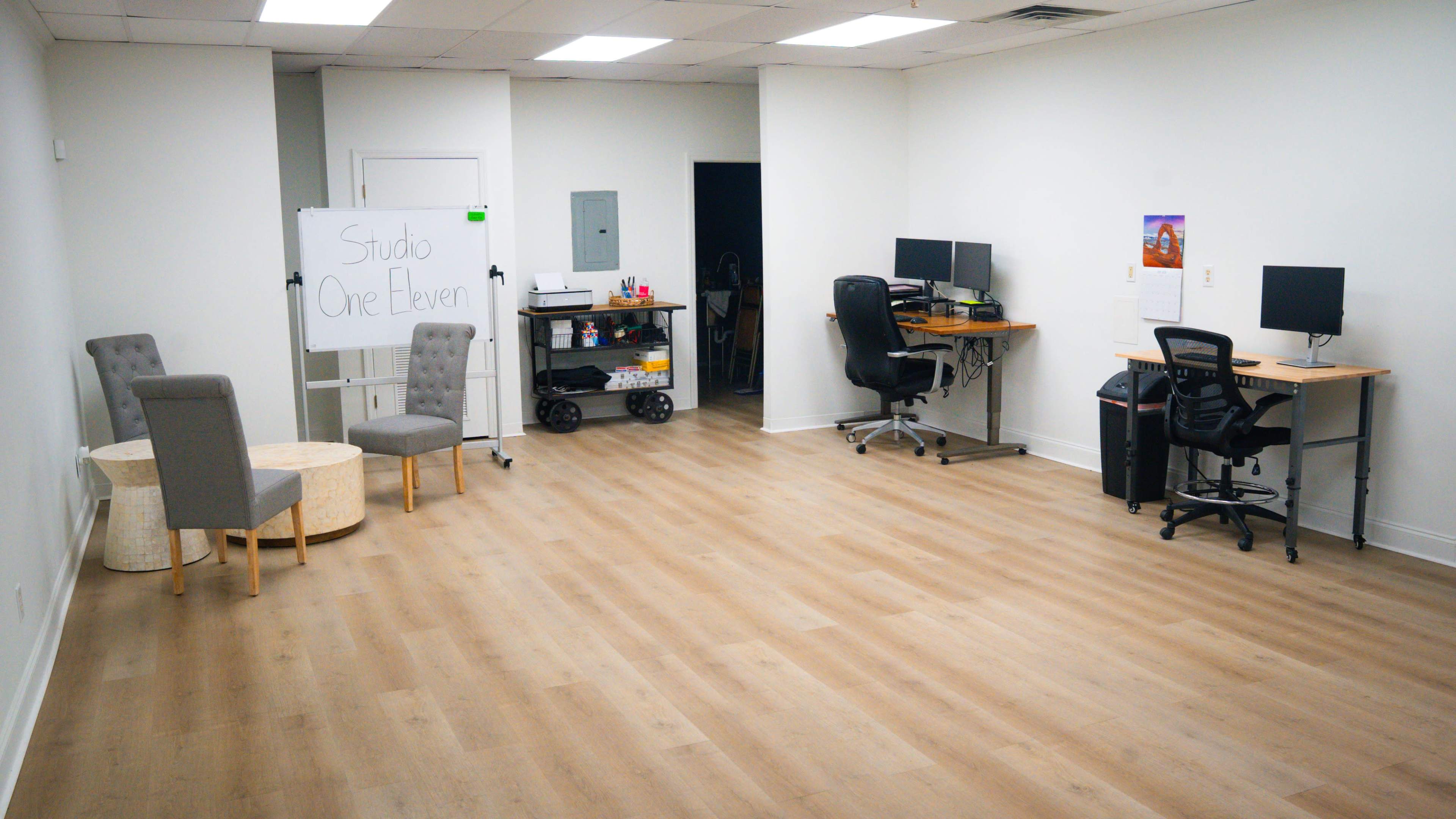 The image shows a spacious office area with two desks, two chairs, a small table, and a whiteboard displaying "Studio One Eleven."